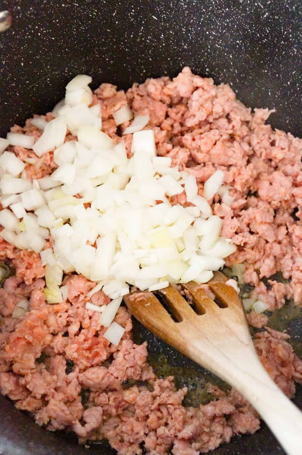 diced onions on top of ground sausage meat in a large pot