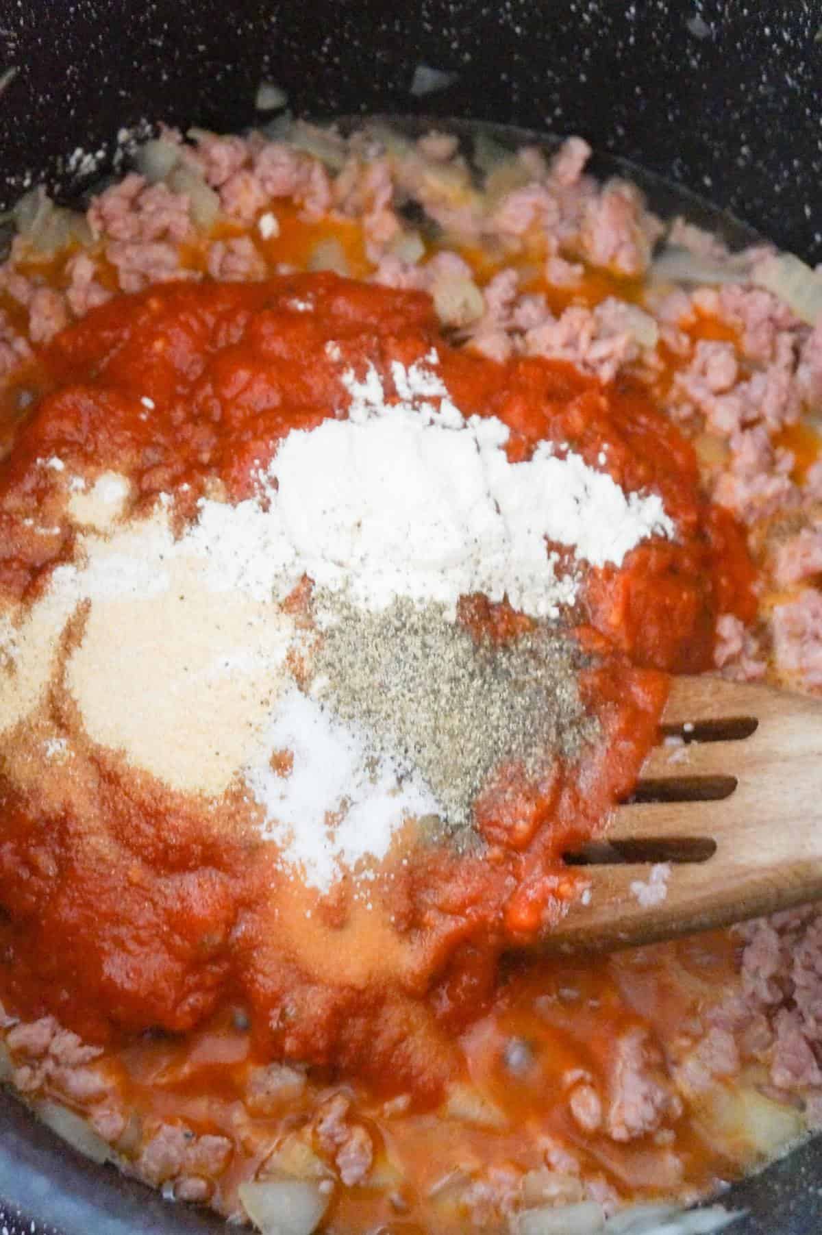 spices and marinara sauce on top of Italian sausage meat in a large pot