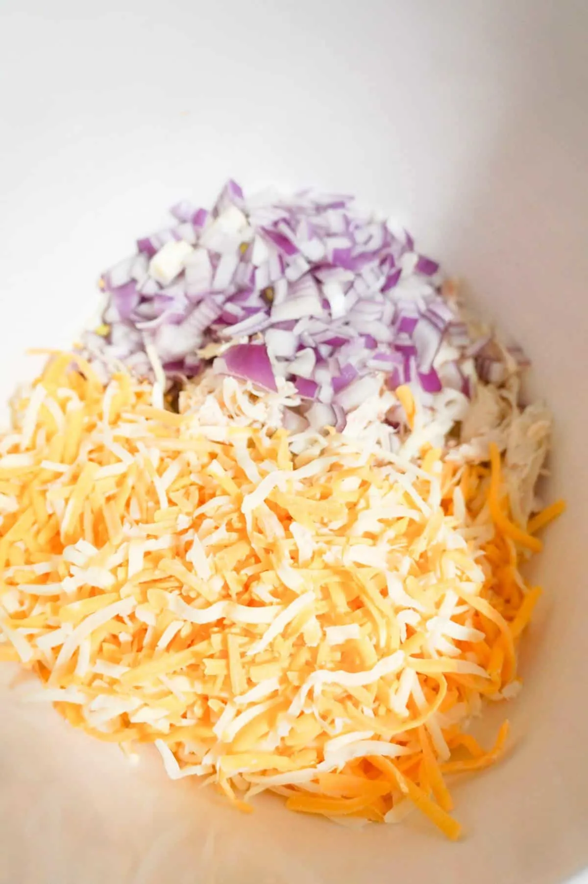 shredded cheese, diced red onion and shredded chicken in a mixing bowl