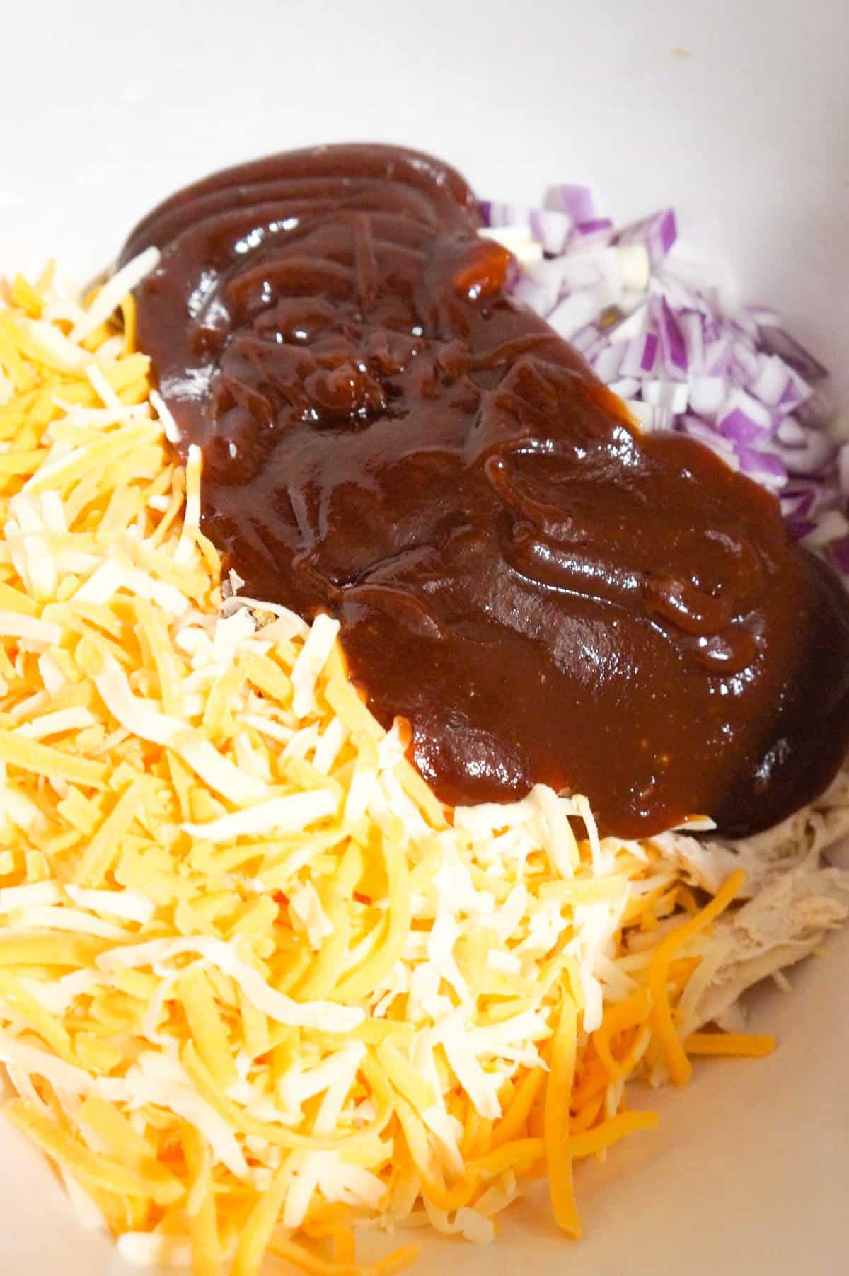 shredded cheese, bbq sauce and diced red onion on top of shredded chicken in a mixing bowl