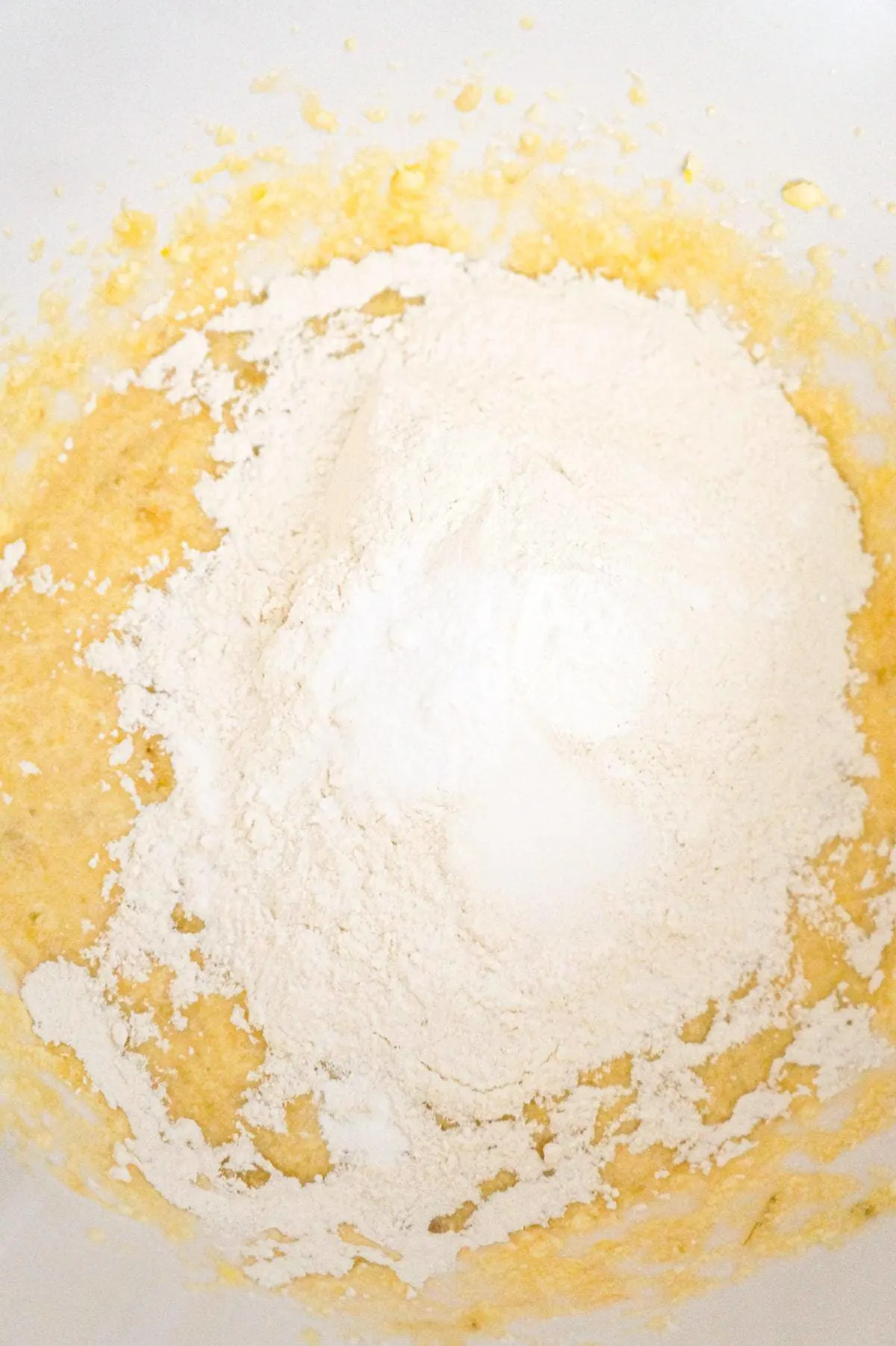 flour, baking powder, baking soda and salt on top of a creamy banana mixture in a mixing bowl