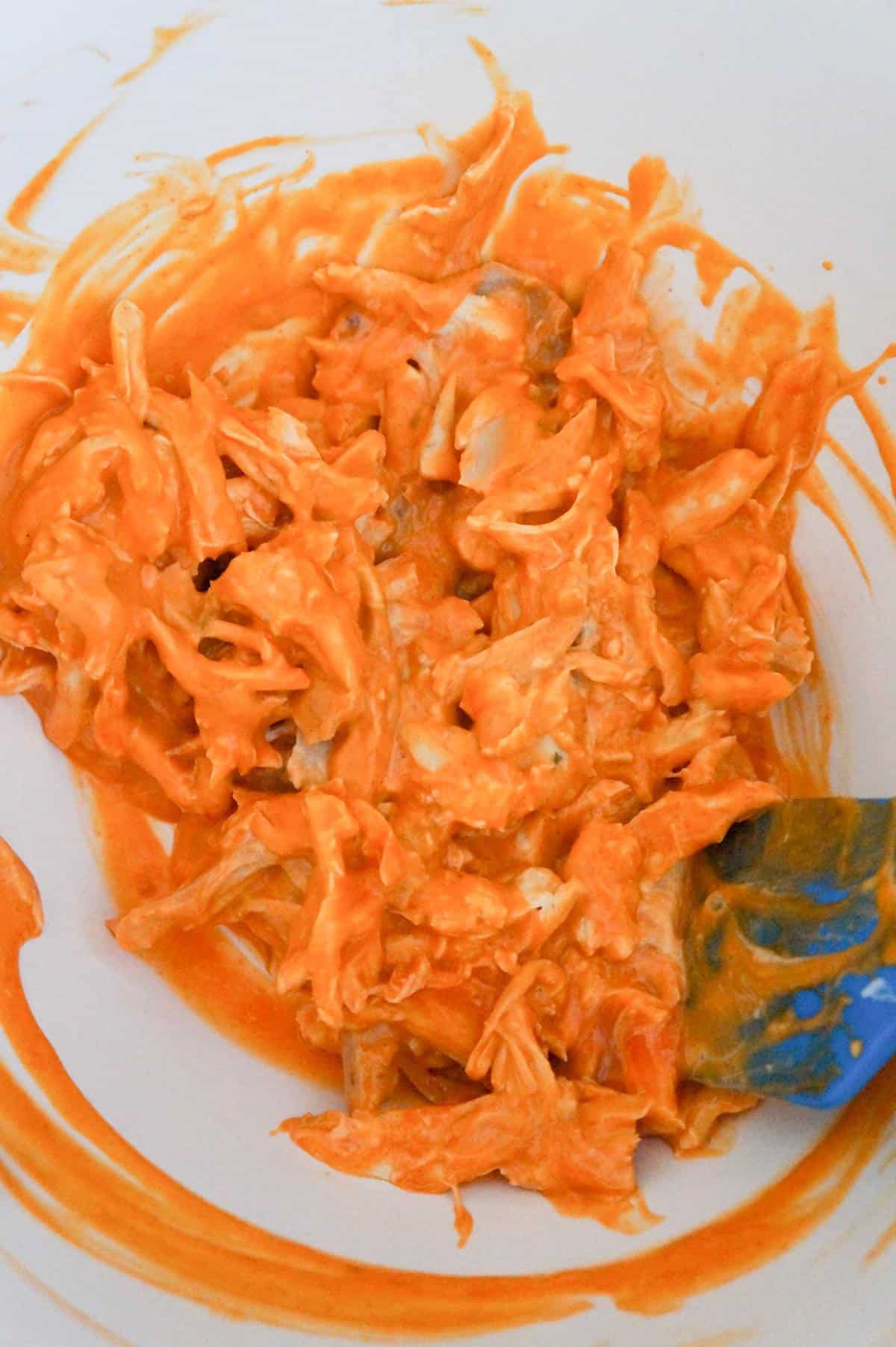 shredded chicken tossed in buffalo sauce in a mixing bowl