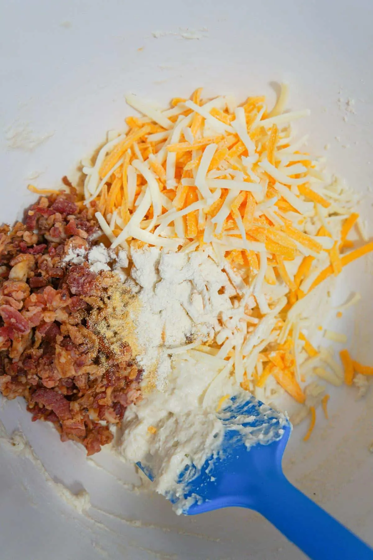 shredded cheese, crumbled bacon and spices on top of biscuit dough in a mixing bowl