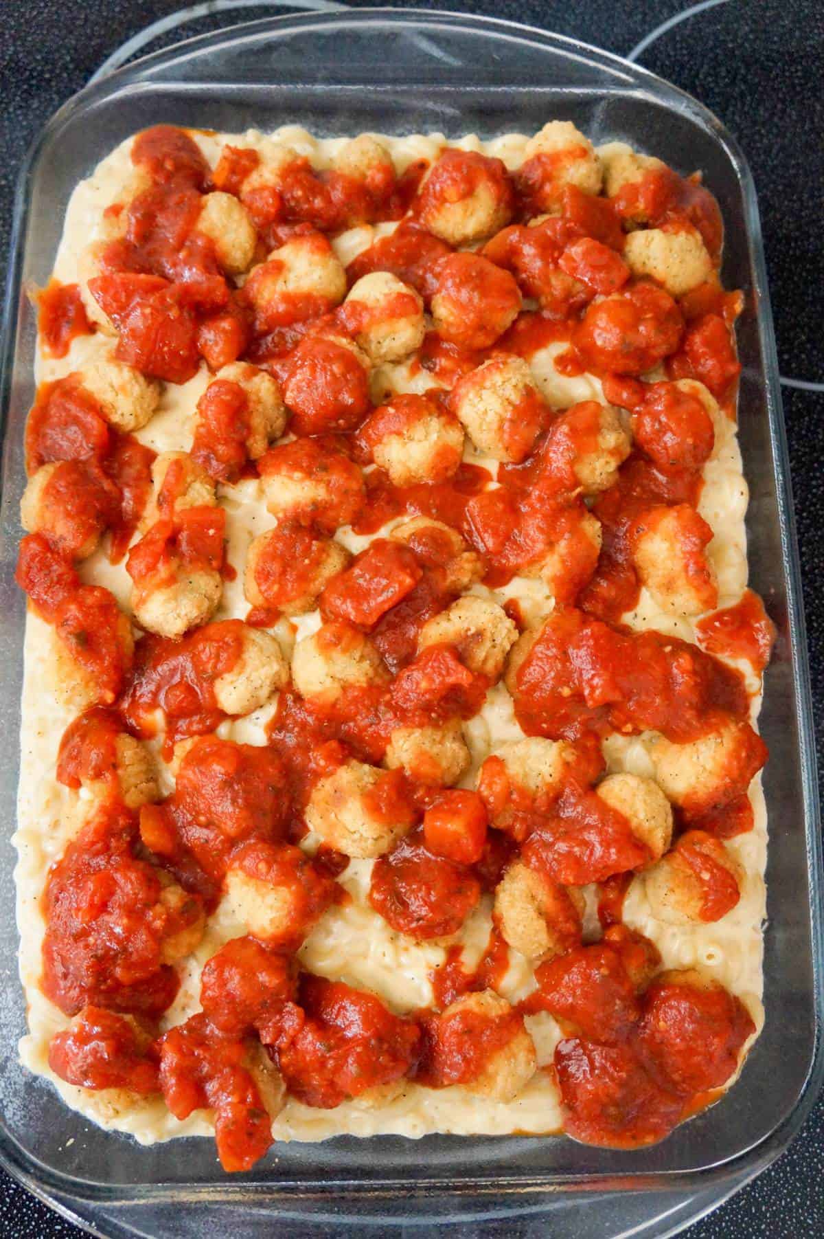 marinara sauce and popcorn chicken on top of mac and cheese in a baking dish