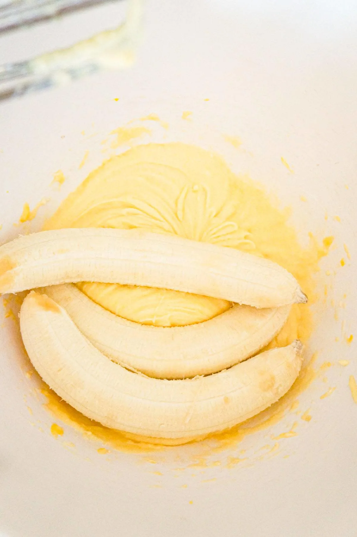 ripe bananas on top of creamed butter and sugar mixture in a mixing bowl