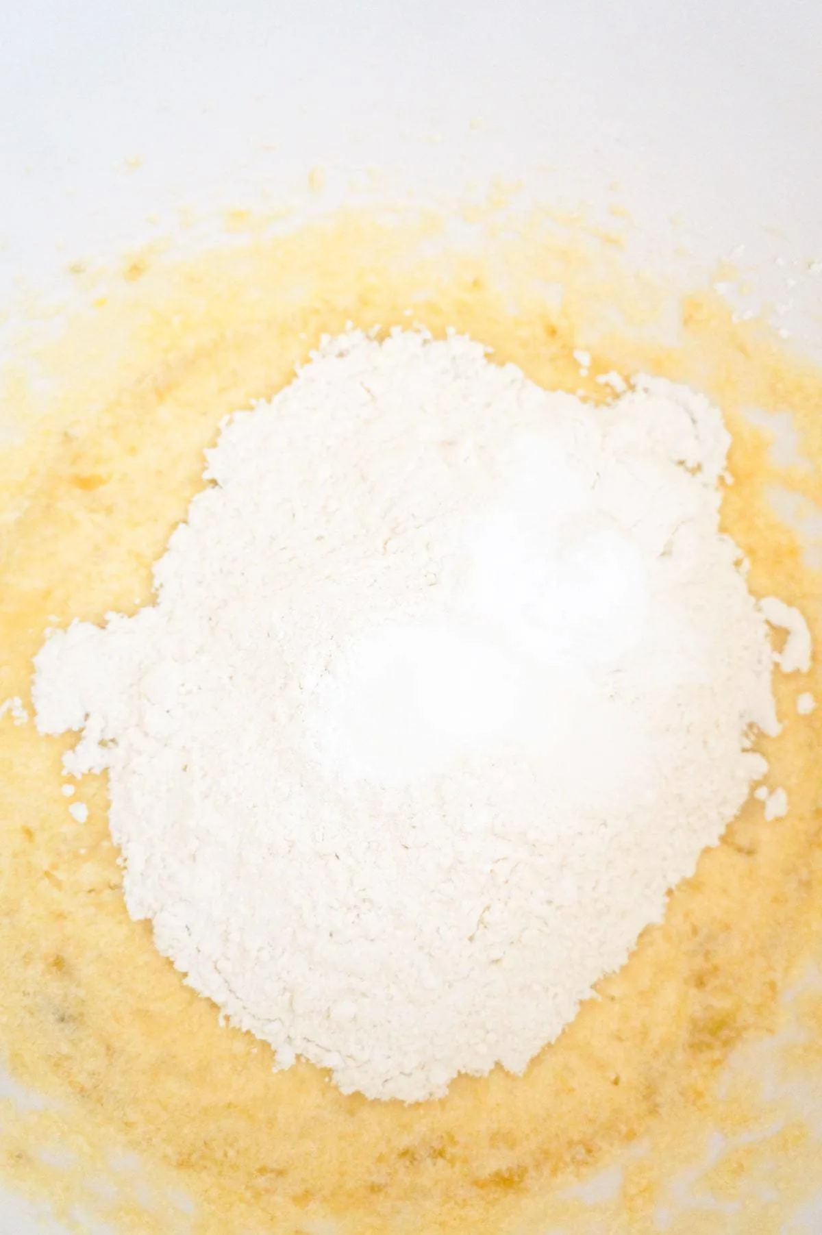 flour, baking soda, baking powder and salt on top of creamy banana mixture in a mixing bowl