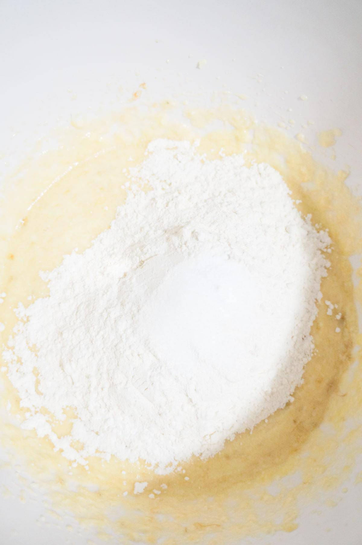 flour, baking soda, baking powder and salt on top of creamy banana mixture in a mixing bowl