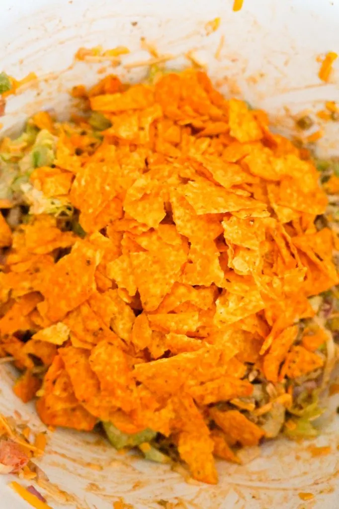 crumbled Doritos on top of salad in a mixing bowl