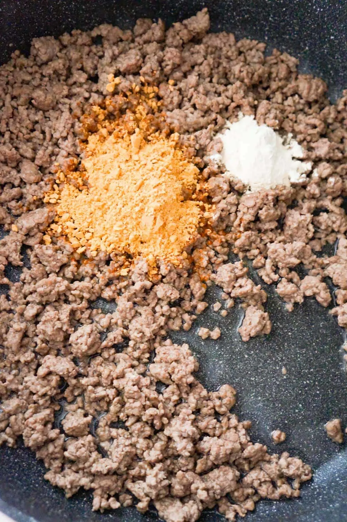 taco seasoning and onion powder on top of cooked ground beef in a pan