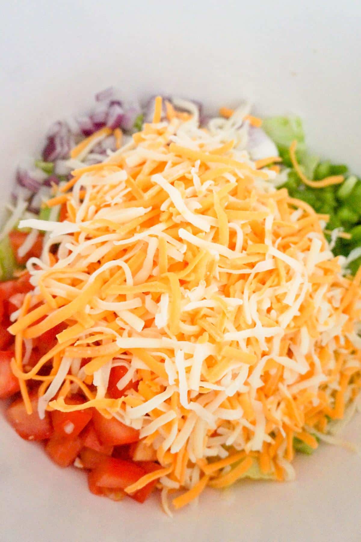 shredded cheese on top of salad in a mixing bowl