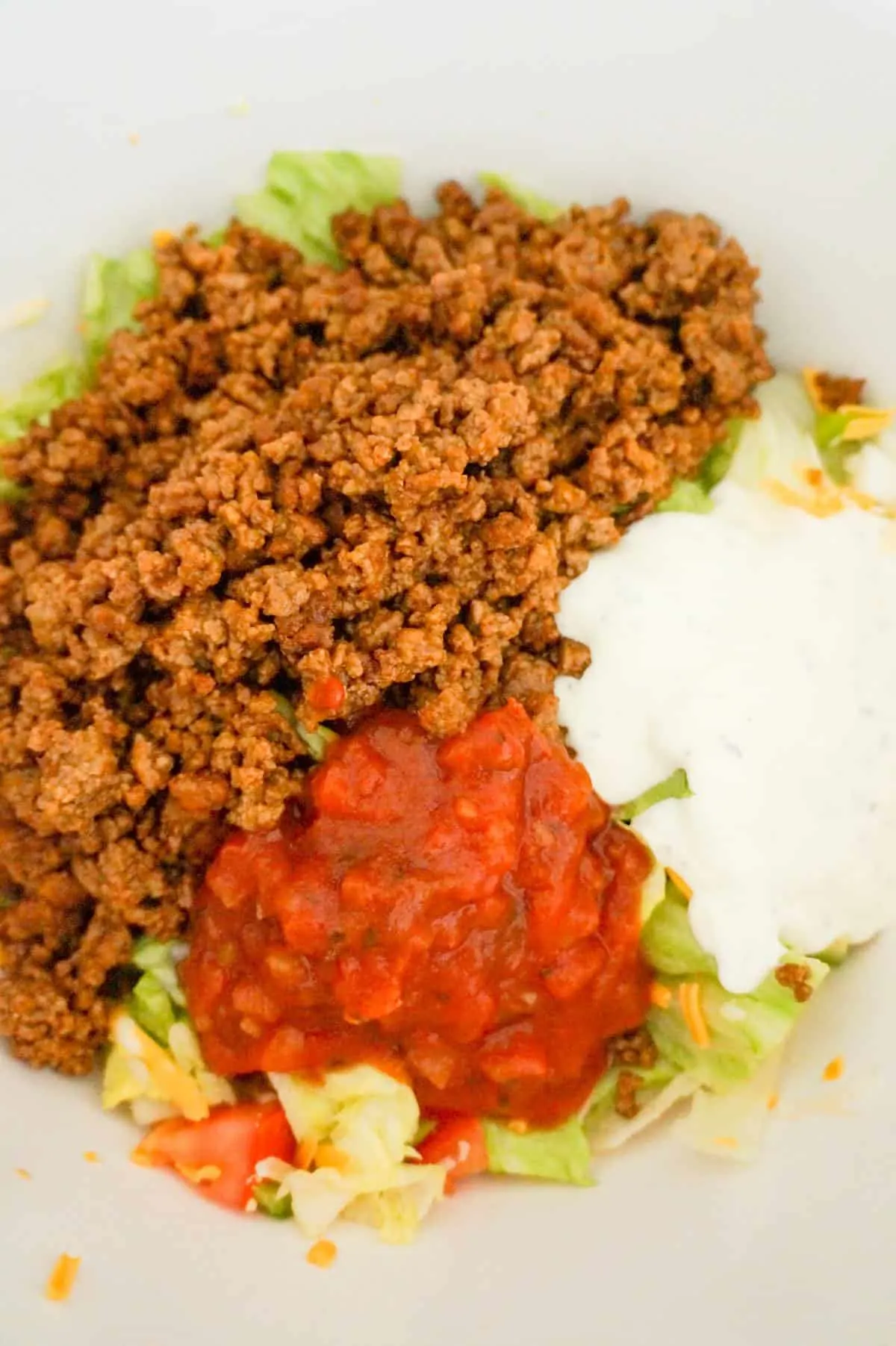 beef taco meat, salsa and ranch dressing on top of salad in a mixing bowl