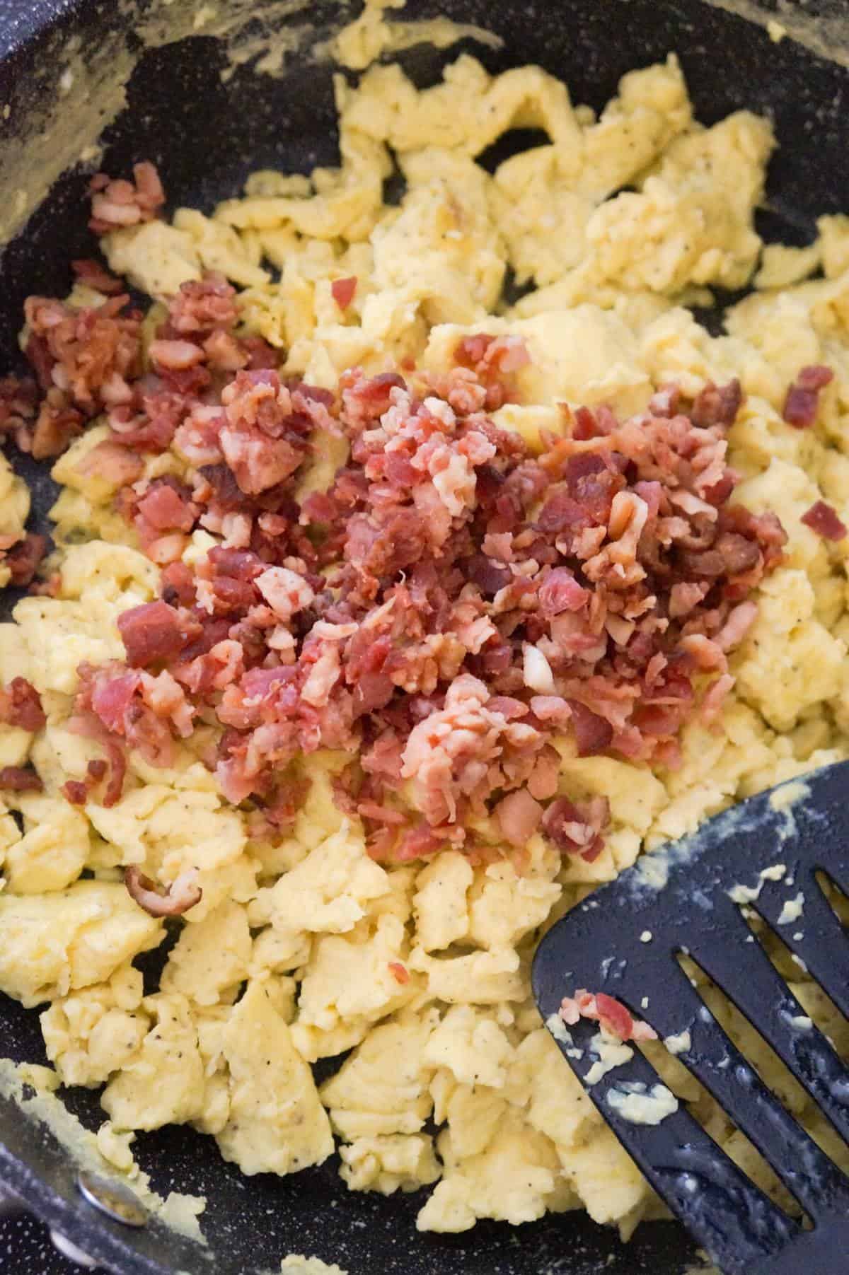 crumbled bacon on top of scrambled eggs in a saute pan