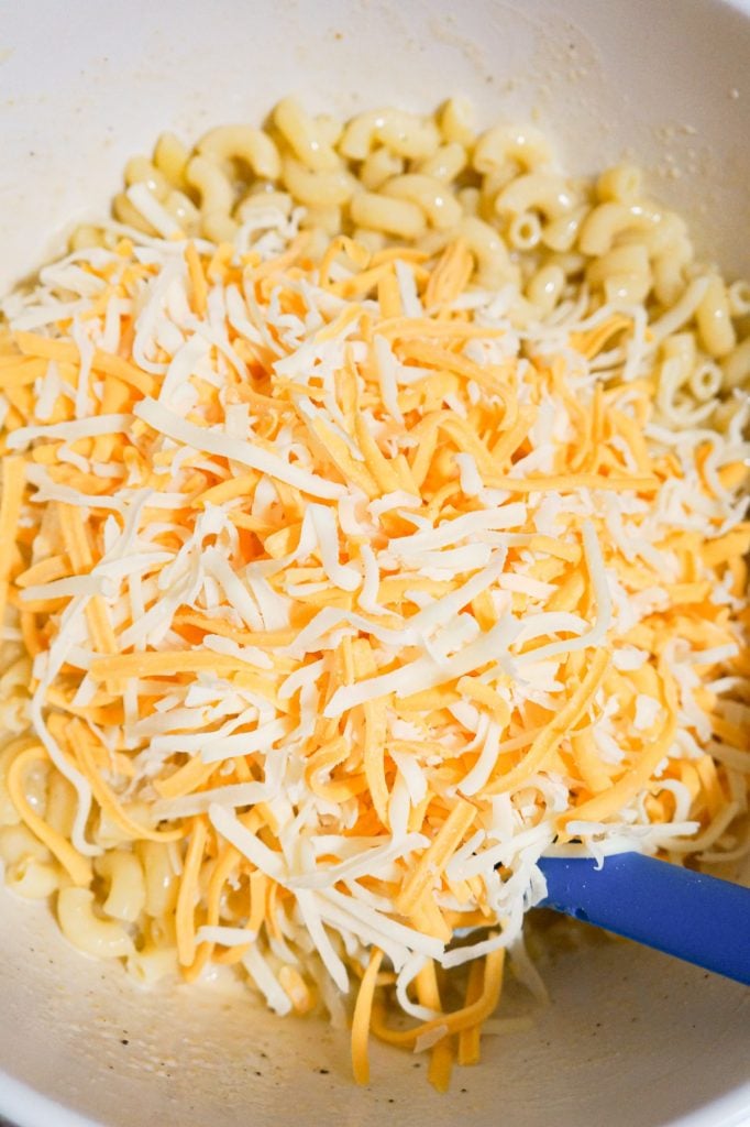 shredded cheese on top of macaroni in a mixing bowl