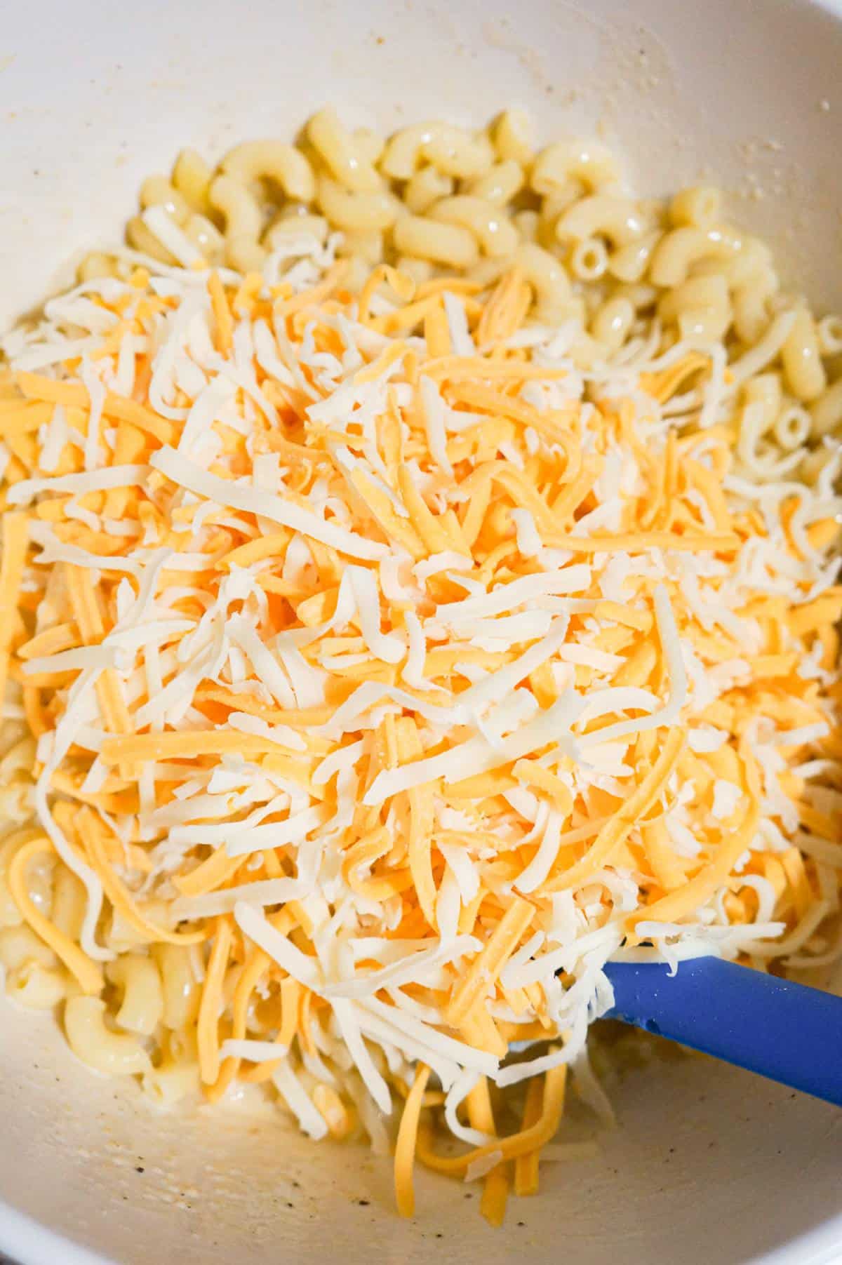 shredded cheese on top of macaroni in a mixing bowl