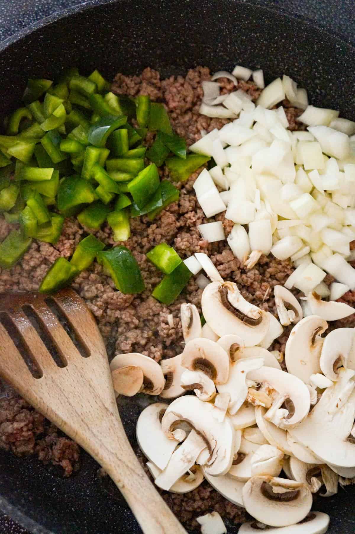 diced green pepper, diced yellow onion and sliced mushrooms on top of ground beef in a saute pan