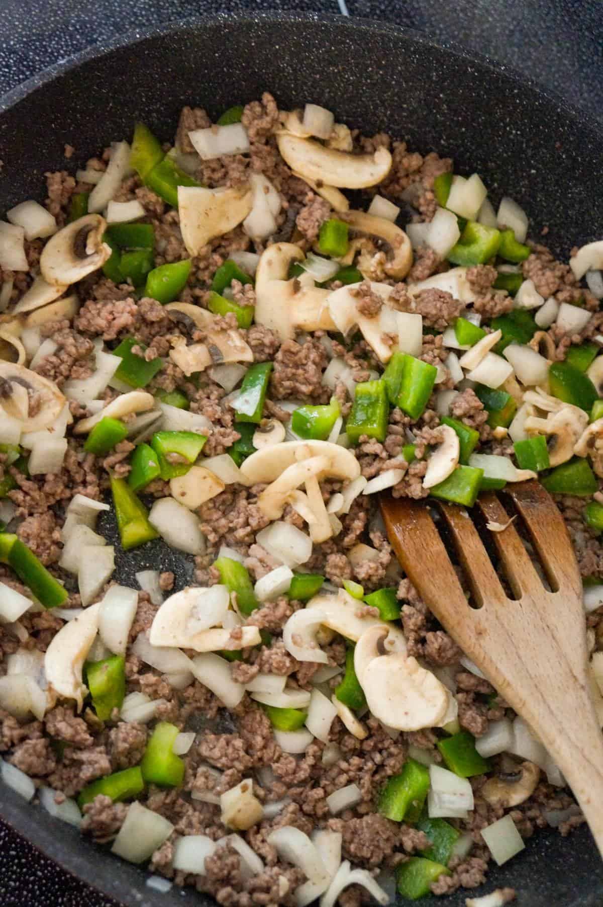 sliced mushrooms, diced green peppers and ground beef cooking in a saute pan