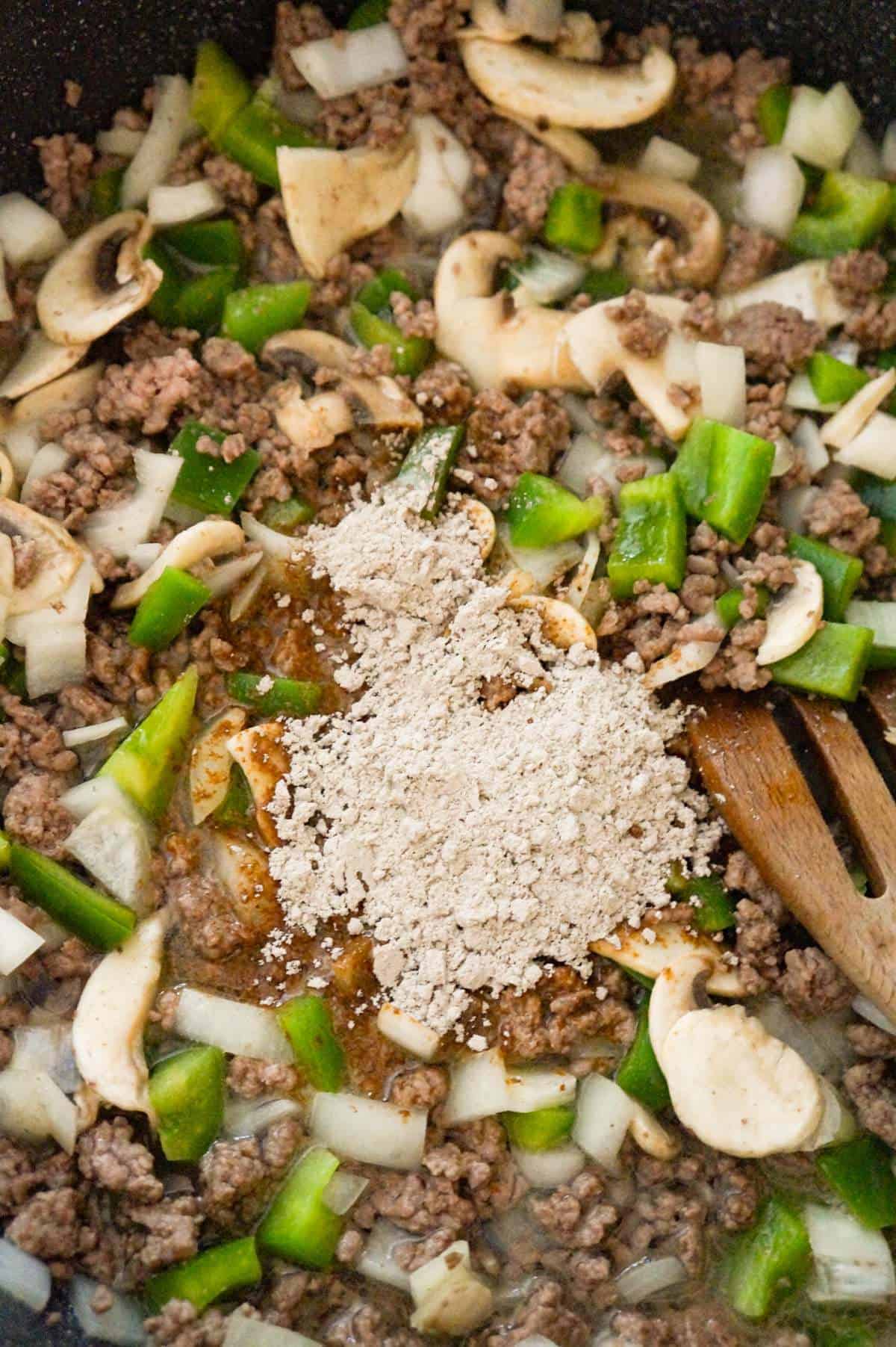 gravy mix on top of sliced mushrooms, diced green peppers and ground beef in a saute pan