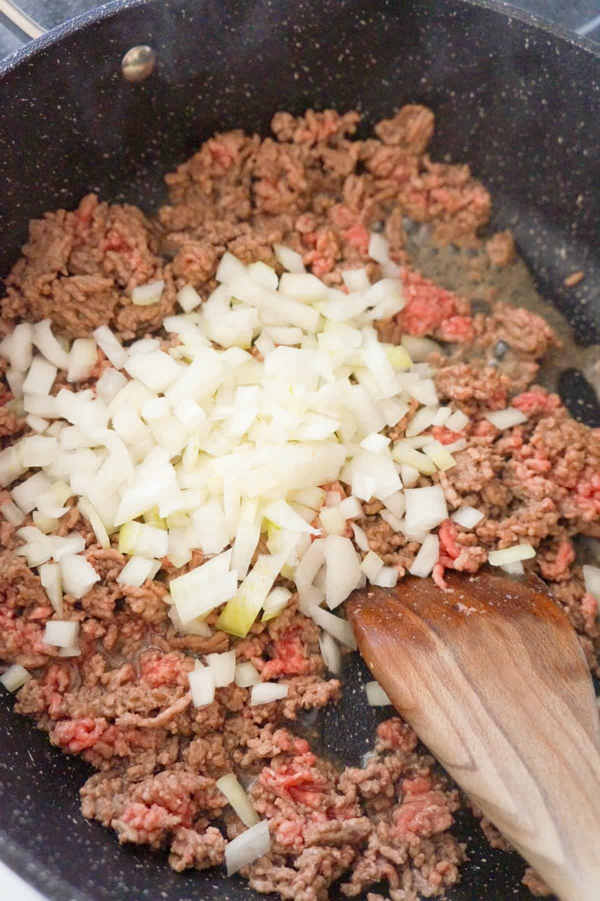 diced onions on top of ground beef in a saute pan