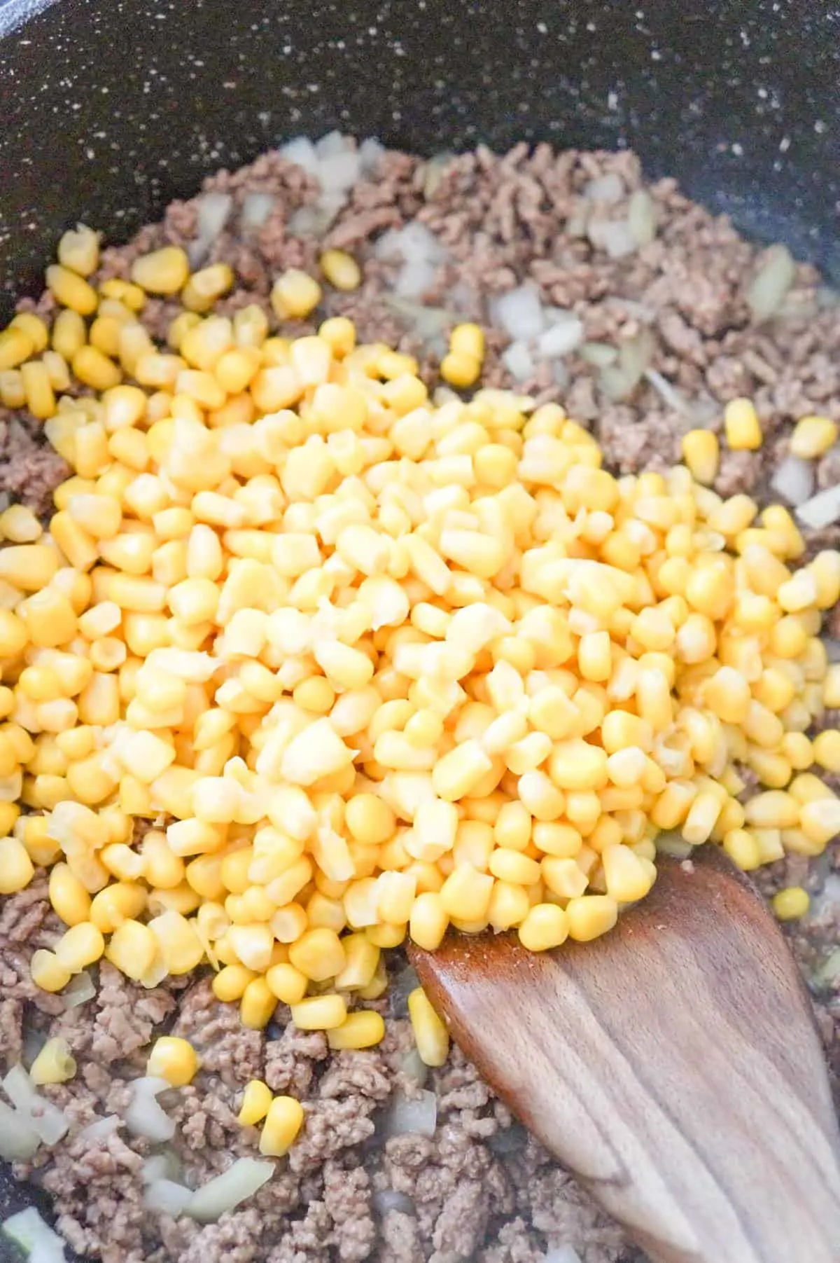 corn on top of cooked ground beef in a saute pan