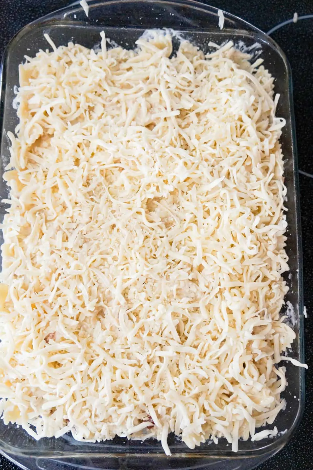 shredded mozzarella on top of Alfredo pasta in a baking dish
