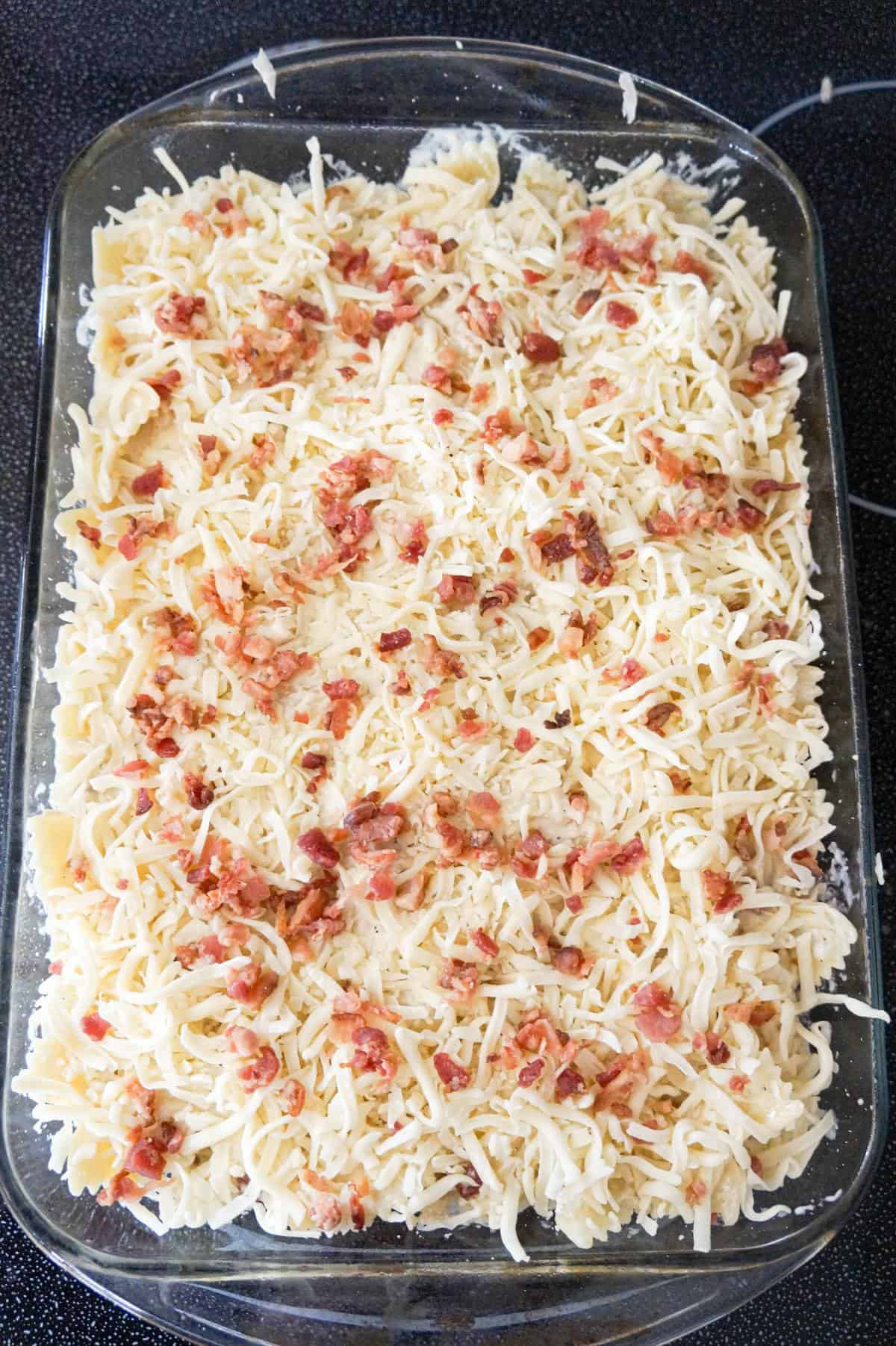 crumbled bacon and shredded mozzarella cheese on top of Alfredo pasta in a baking dish