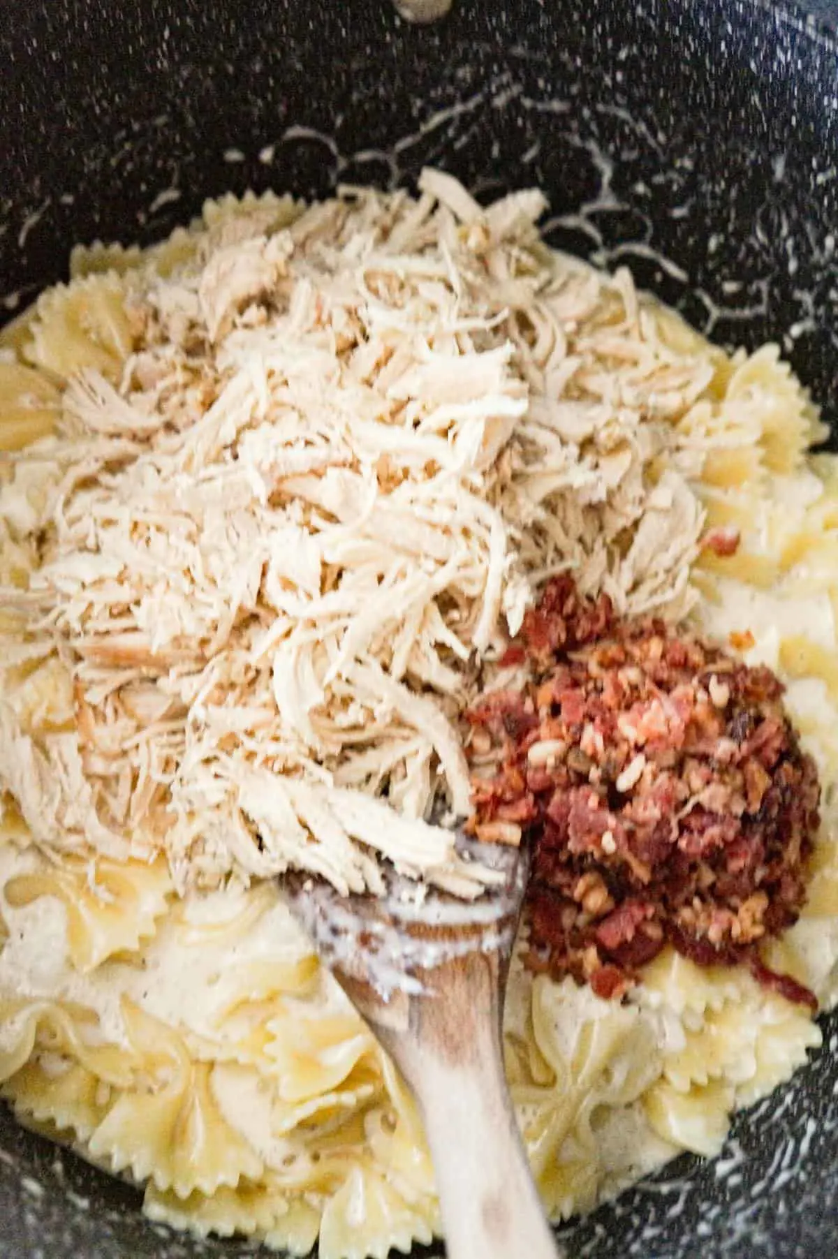 shredded chicken and crumbled bacon on top of creamy bow tie pasta in a large pot