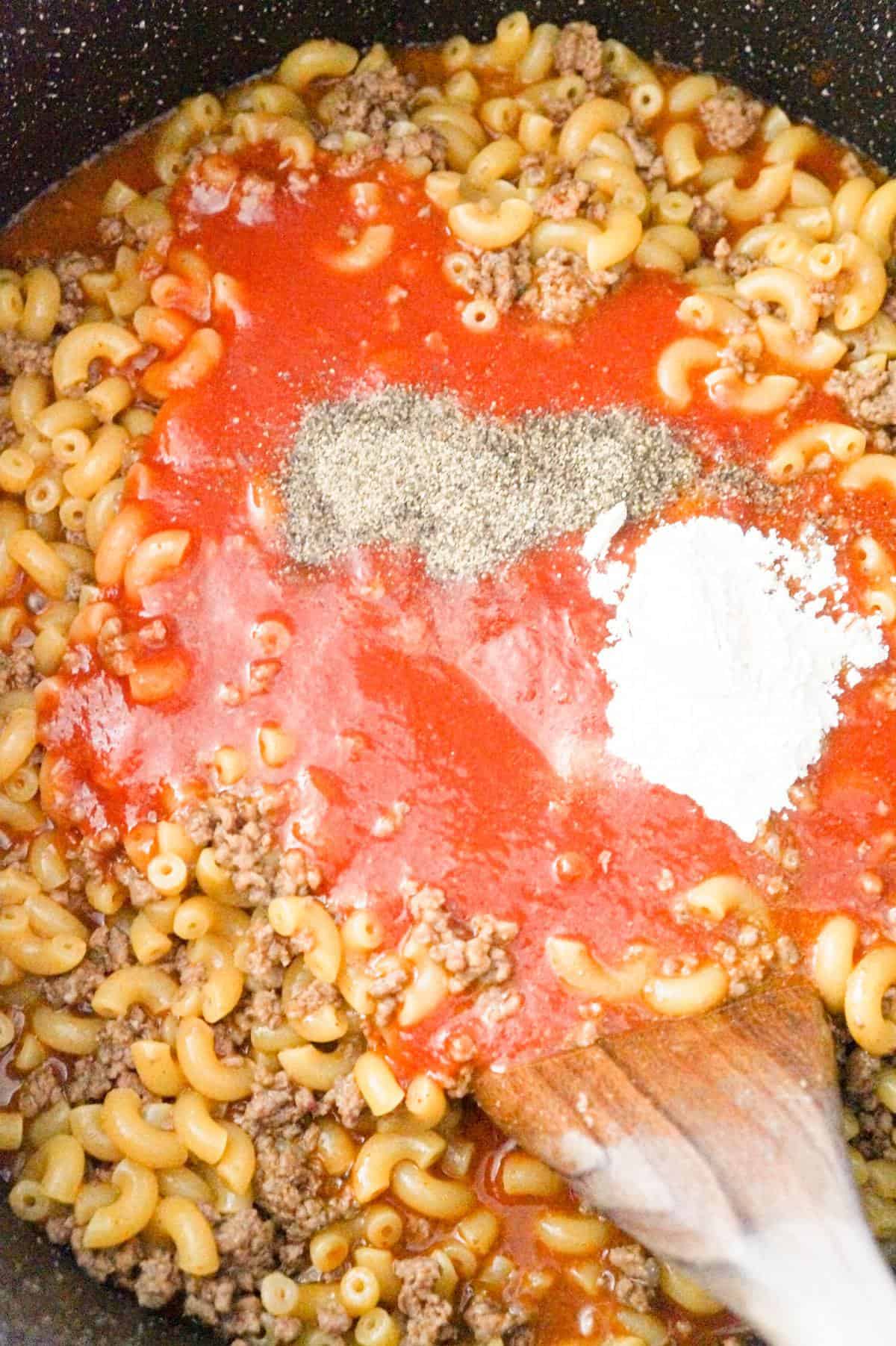 tomato sauce, salsa and spices on top of cooked macaroni and ground beef in a large pot