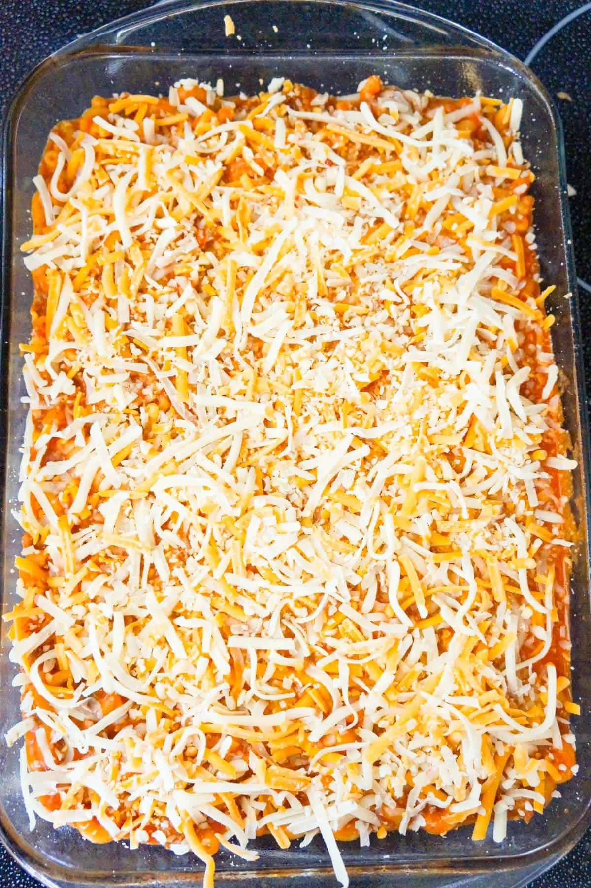 shredded cheese on top of chili mac in a baking dish