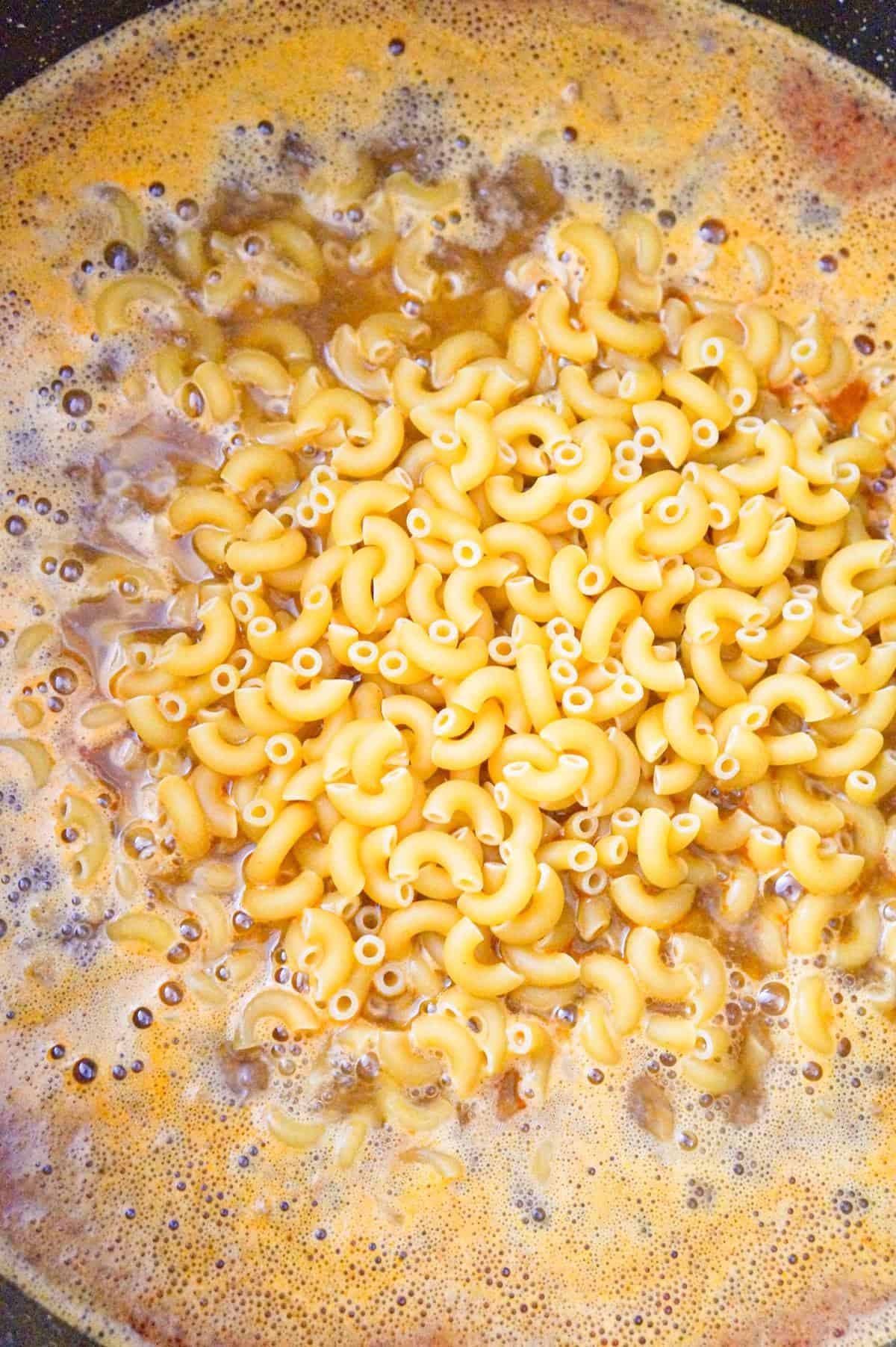 uncooked macaroni noodles on top of water, chili seasoning and ground beef in a large pot