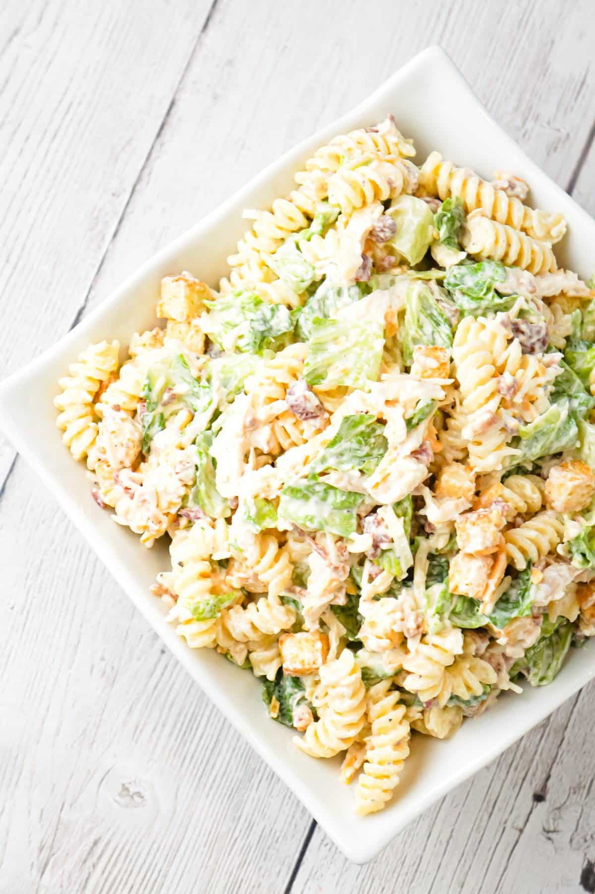 Chicken Caesar Pasta Salad is a tasty side cold dish recipe loaded with chopped romaine, shredded chicken, crumbled bacon, croutons, shredded mozzarella, cheddar and Parmesan cheese all tossed in a creamy garlic Parmesan dressing.