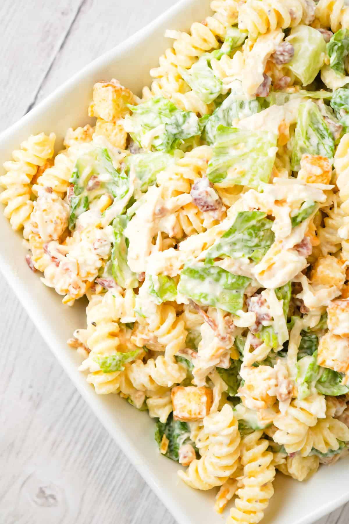 Chicken Caesar Pasta Salad is a tasty side cold dish recipe loaded with chopped romaine, shredded chicken, crumbled bacon, croutons, shredded mozzarella, cheddar and Parmesan cheese all tossed in a creamy garlic Parmesan dressing.