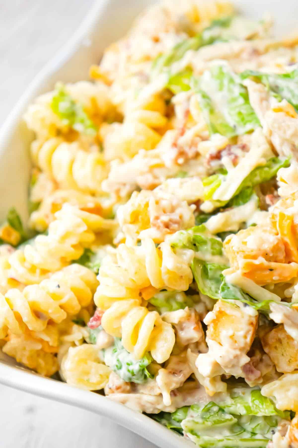 Chicken Caesar Pasta Salad is a tasty side cold dish recipe loaded with chopped romaine, shredded chicken, crumbled bacon, croutons, shredded mozzarella, cheddar and Parmesan cheese all tossed in a creamy garlic Parmesan dressing.