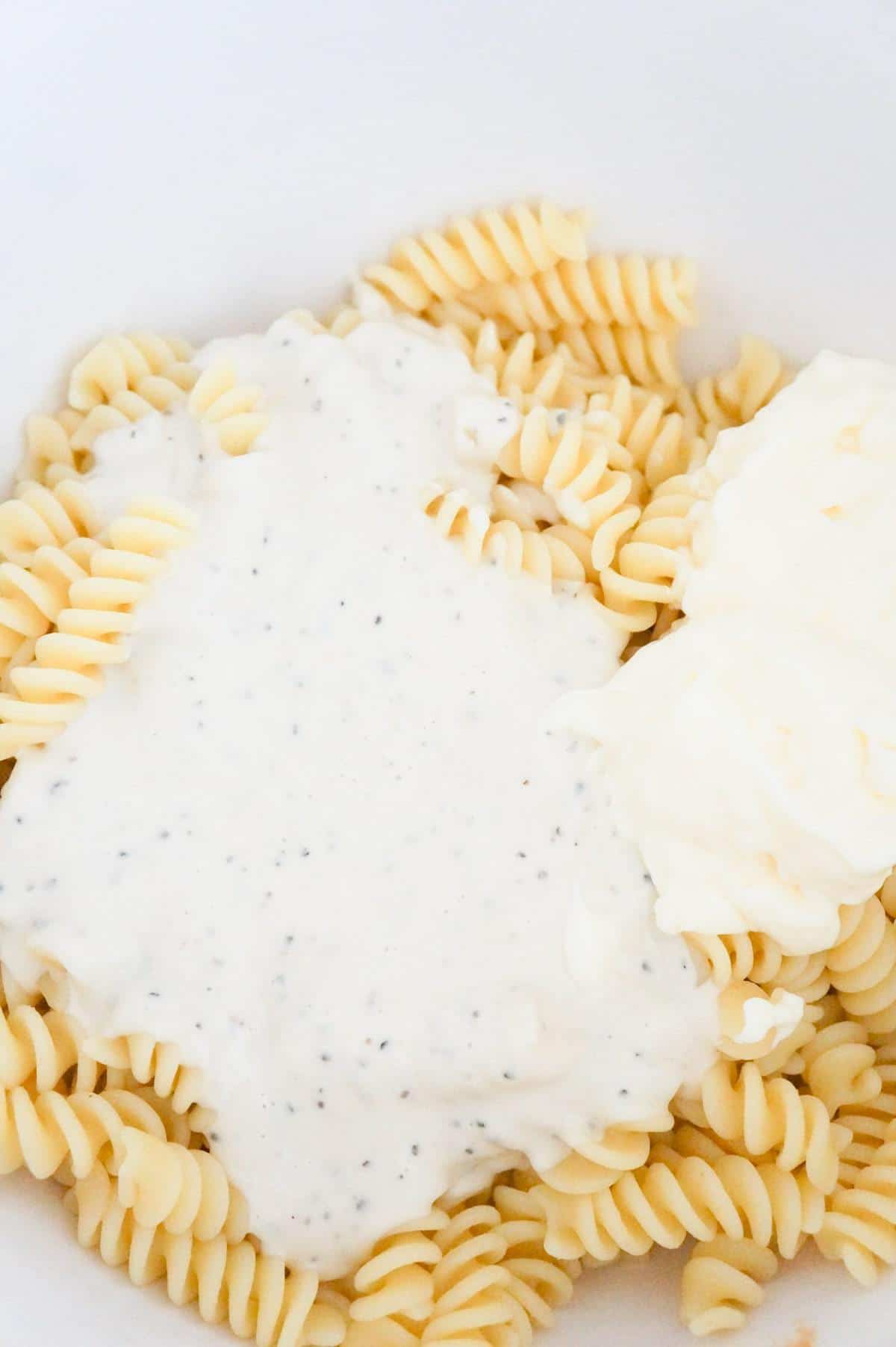 caesar dressing and mayo on top of cooked fusilli noodles in a mixing bowl