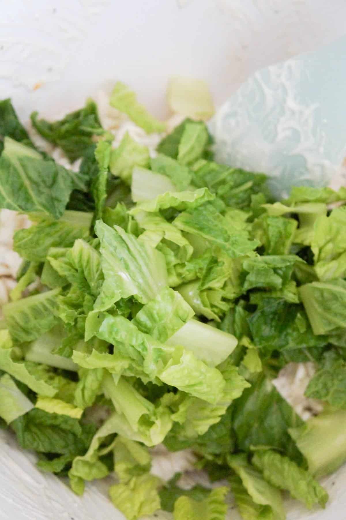 chopped romaine on top of pasta salad in a mixing bowl