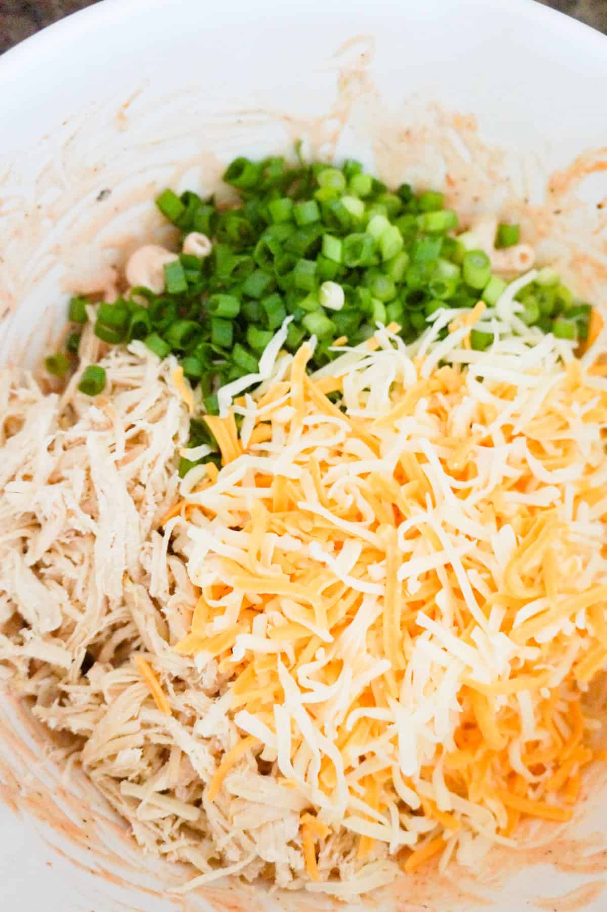 shredded cheese, shredded chicken and chopped green onions on top of pasta in a mixing bowl