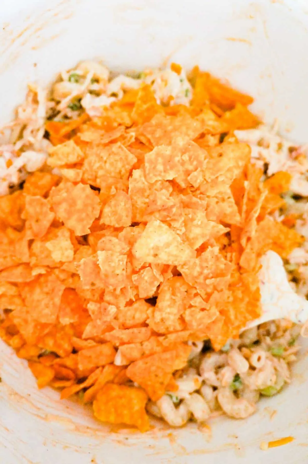 crumbled Doritos on top of pasta salad in a mixing bowl
