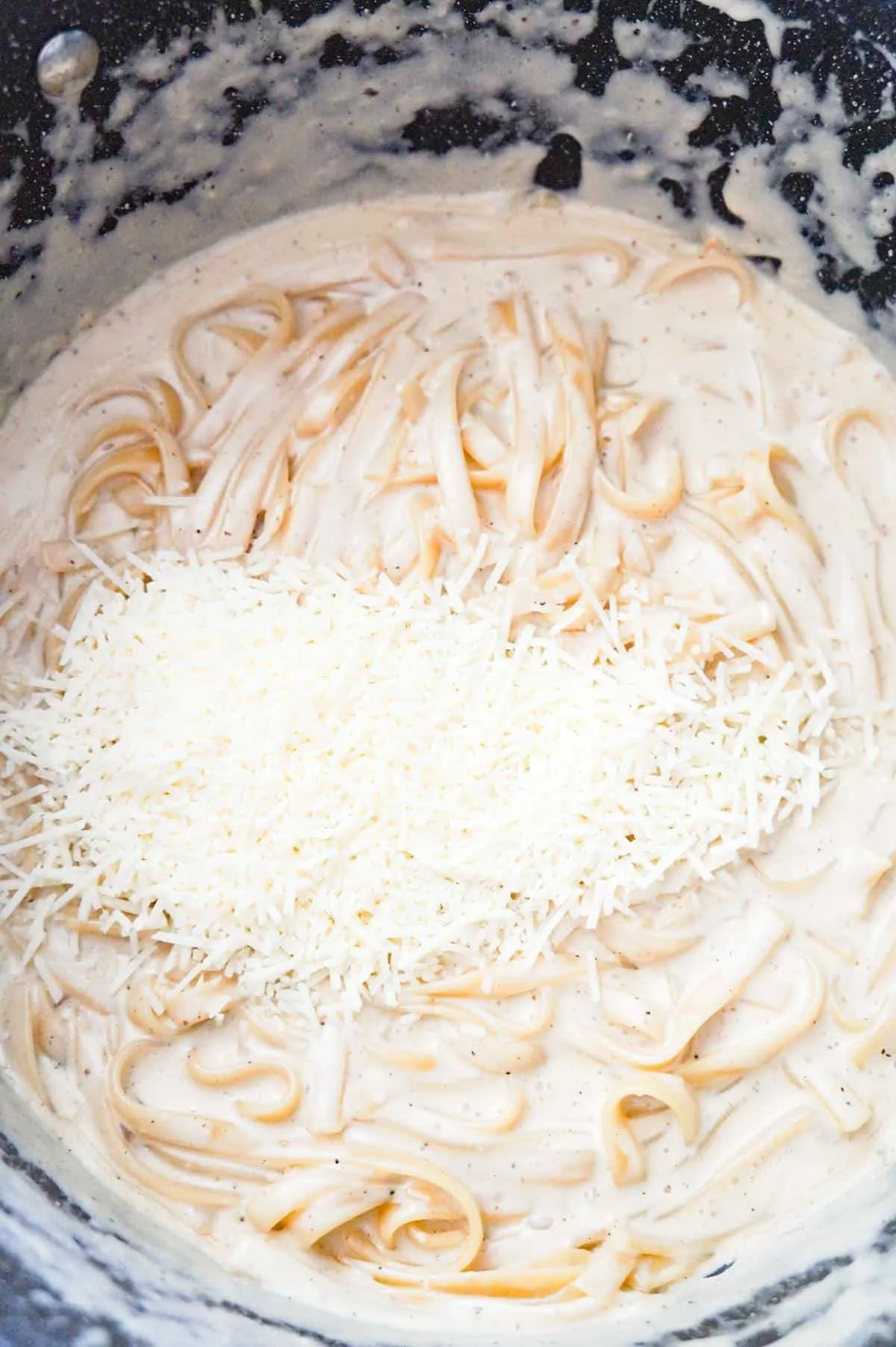 shredded parmesan cheese on top of creamy fettuccine in a large pot