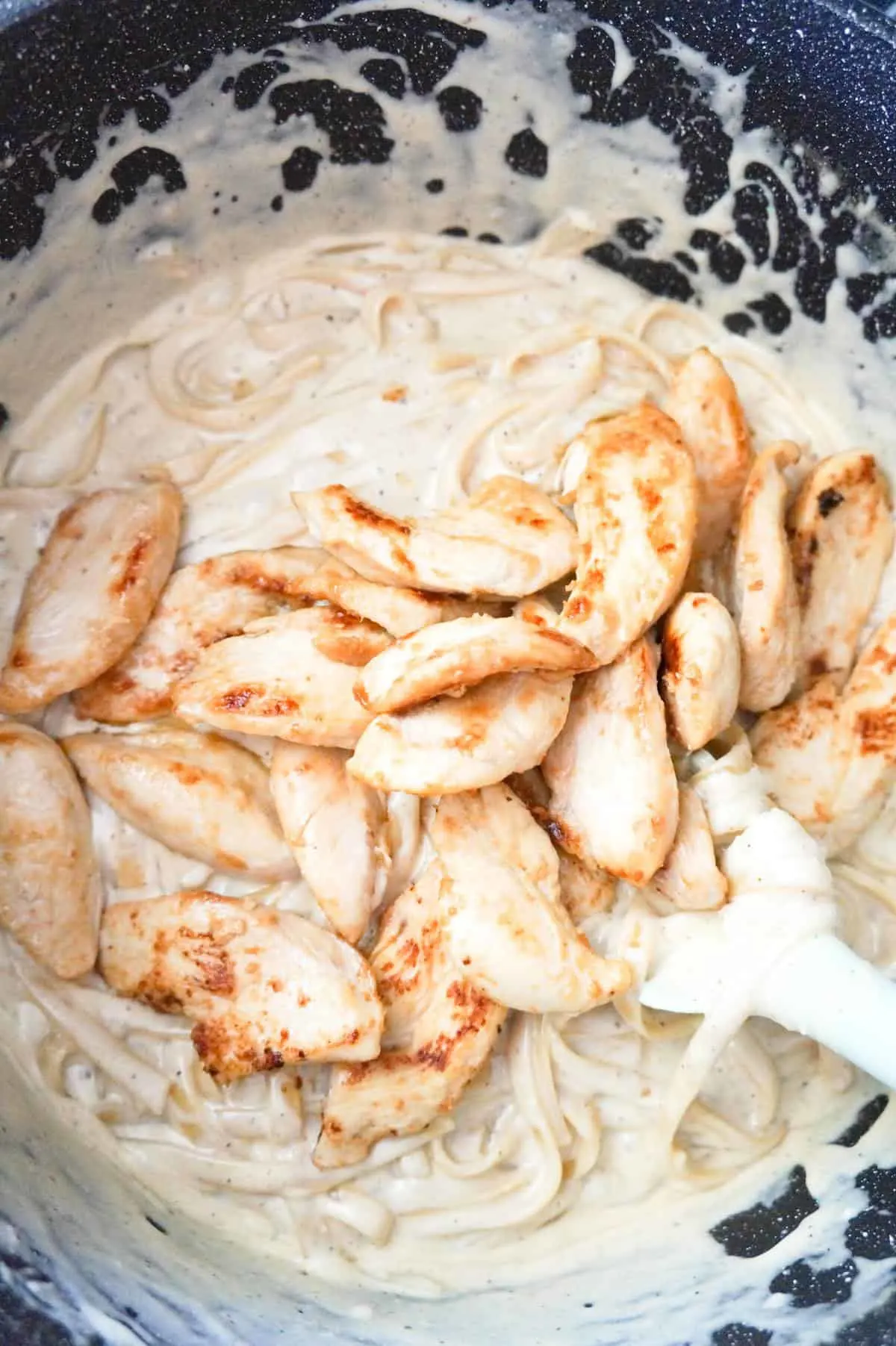 slices of cooked chicken breast on top of fettuccine alfredo in a large pot