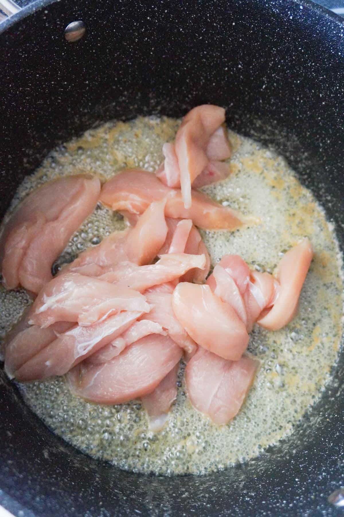 a pile of raw chicken breast slices in a large pot with melted butter