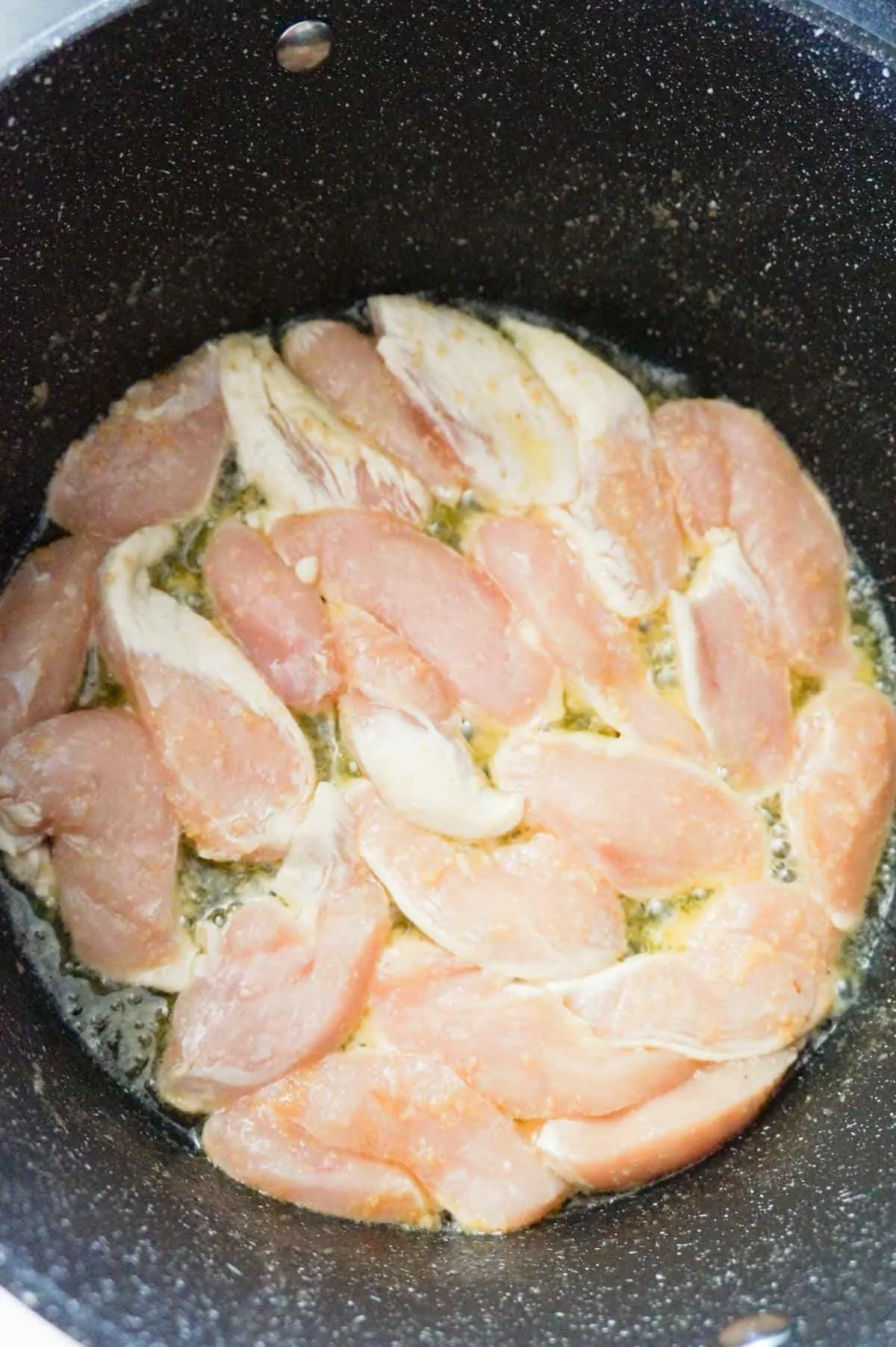 raw chicken breast slices cooking in butter in a large pot
