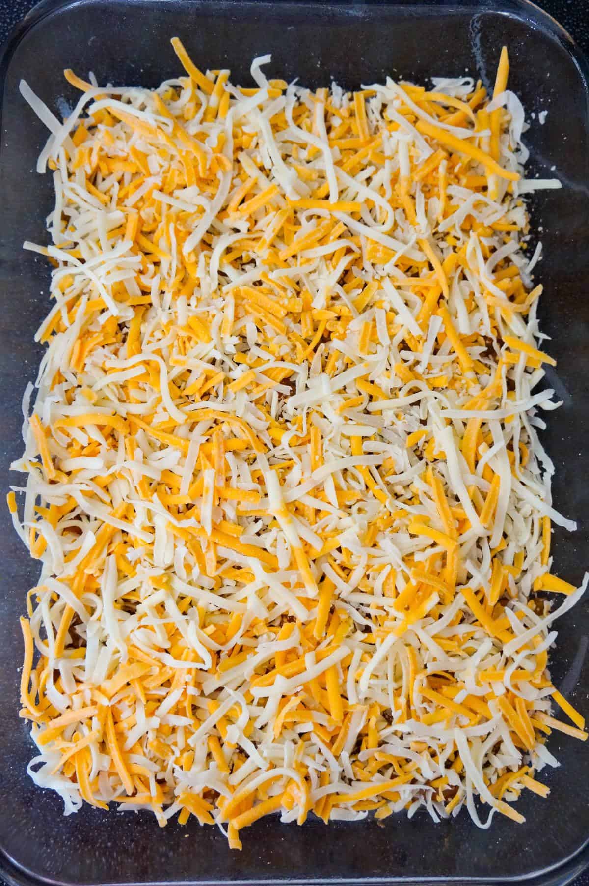 shredded cheese on top of sloppy joe mixture in a baking dish
