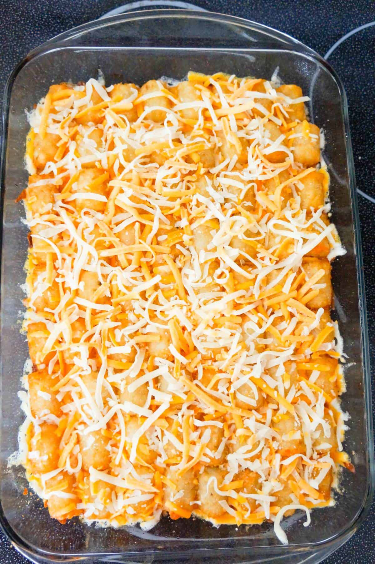 shredded cheese on top of tater tot casserole in a baking dish