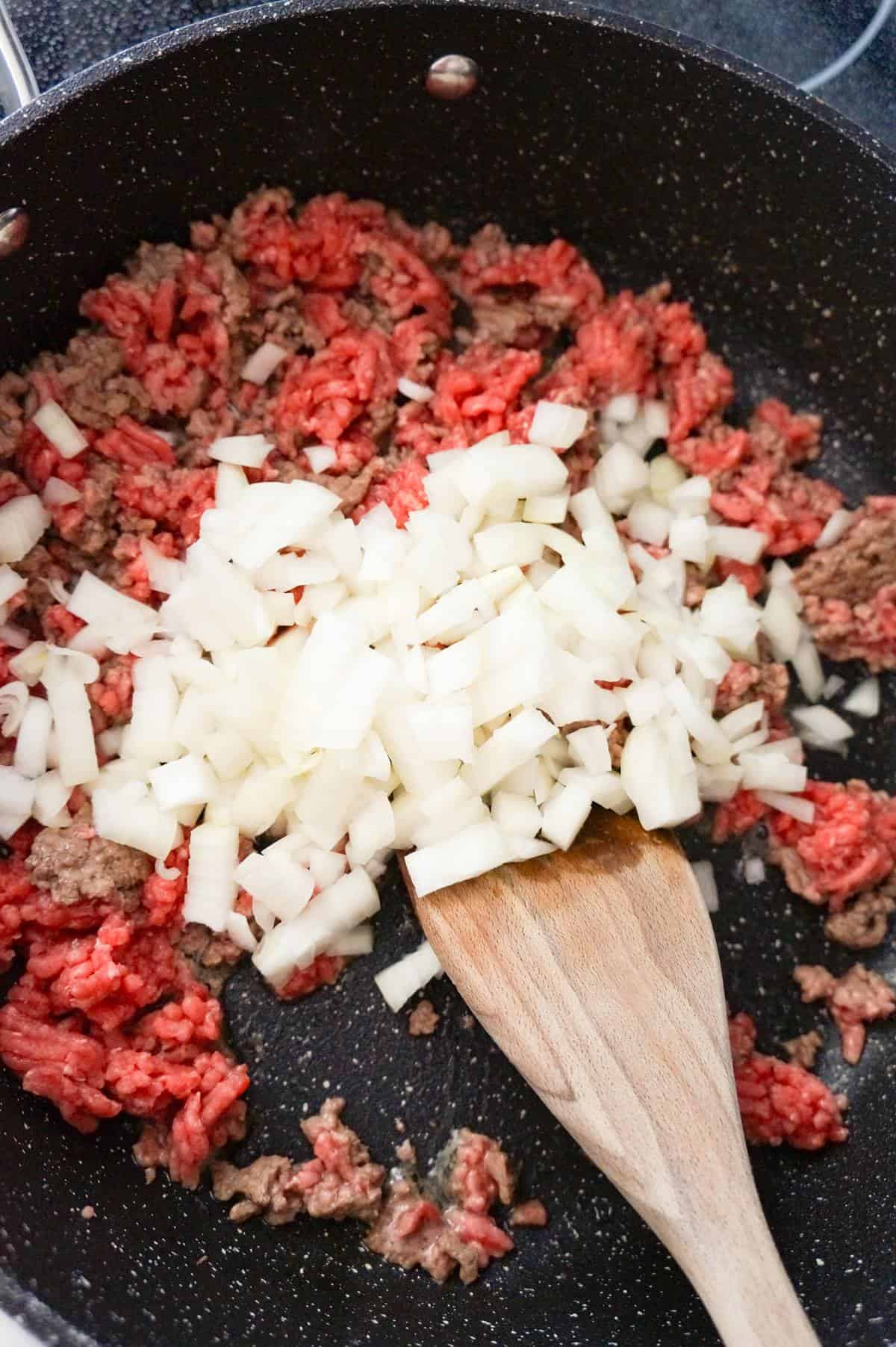 diced onions on top of raw ground beef in a saute pan