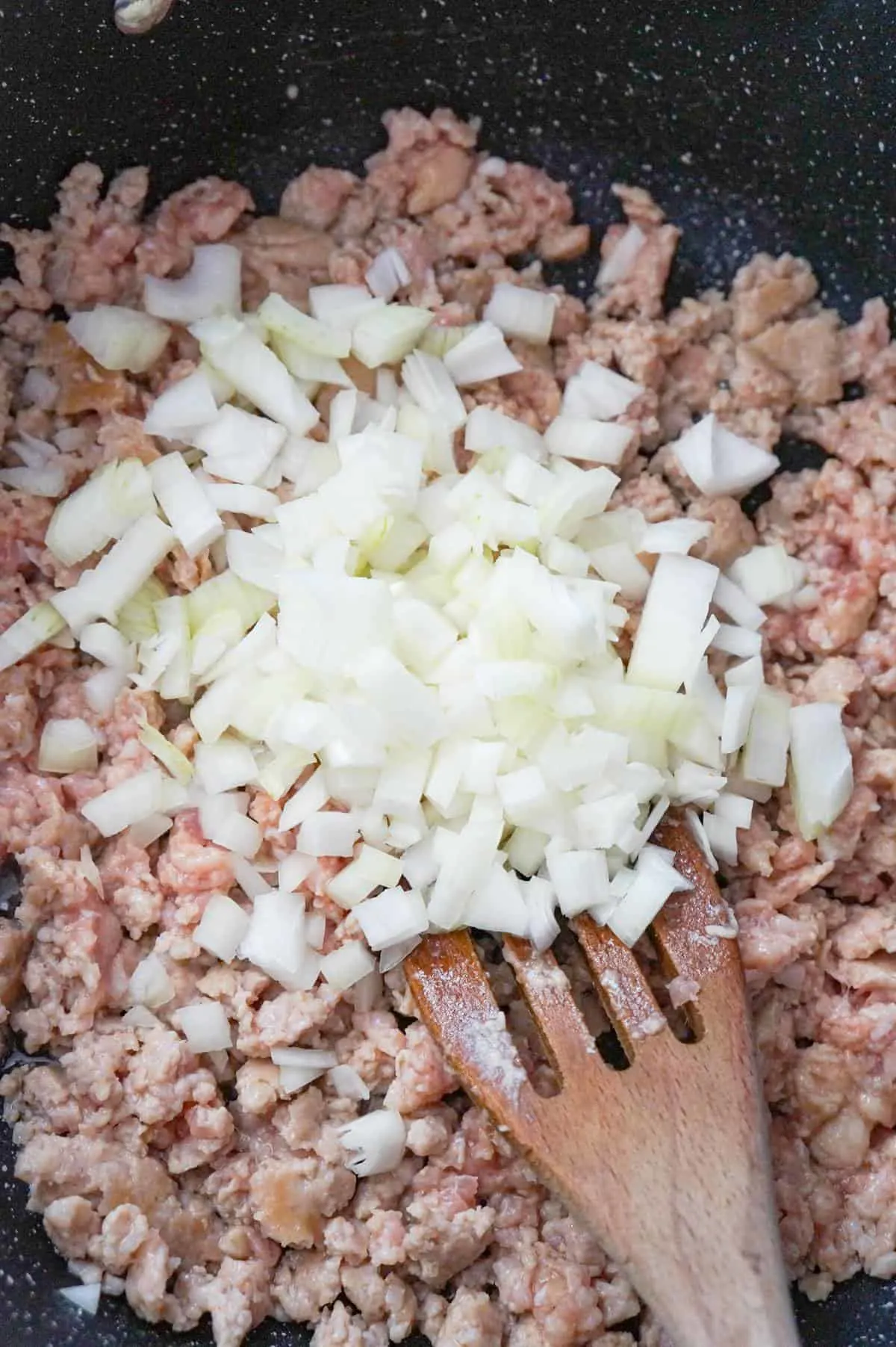 diced onions on top of crumbled sausage meat in a saute pan