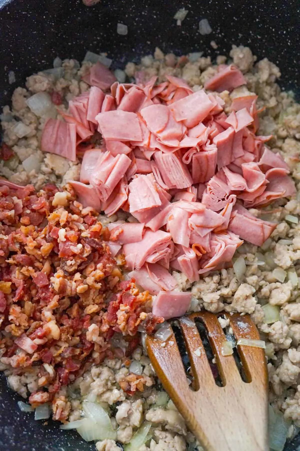 chopped ham and crumbled bacon on top of ground sausage meat in a saute pan