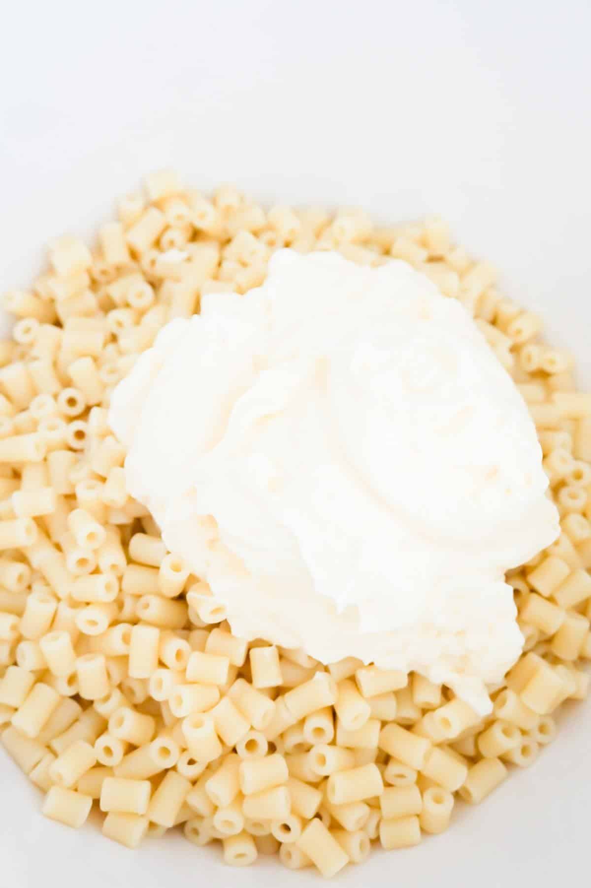 mayo on top of cooked noodles in a mixing bowl