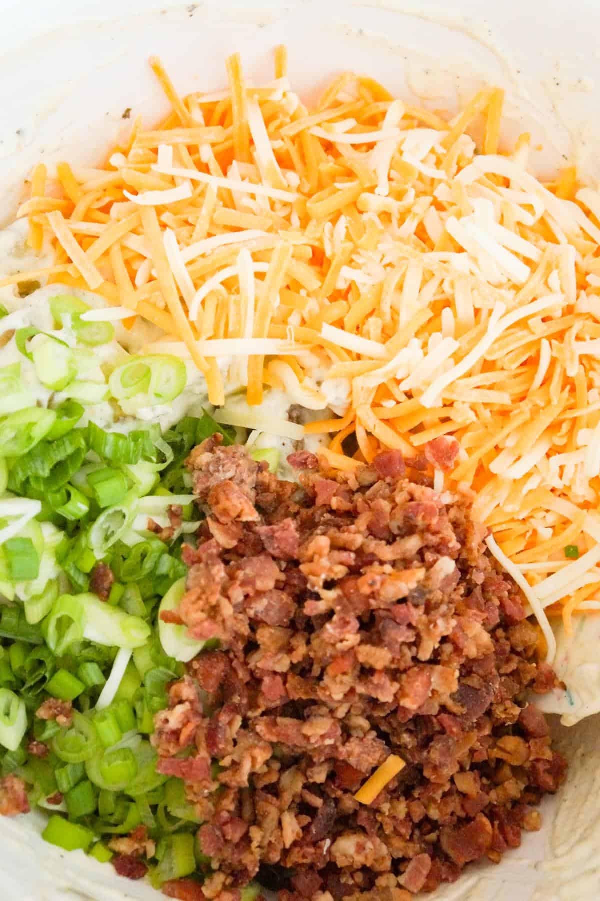 shredded cheddar cheese, chopped green onions and crumbled bacon on top of potato salad in a mixing bowl