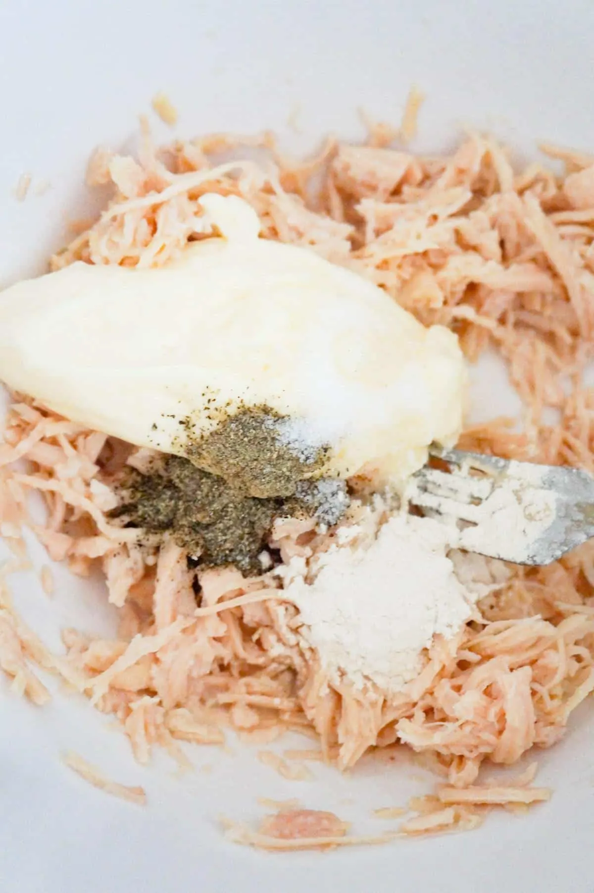 spices and mayo on top of shredded chicken in a mixing bowl