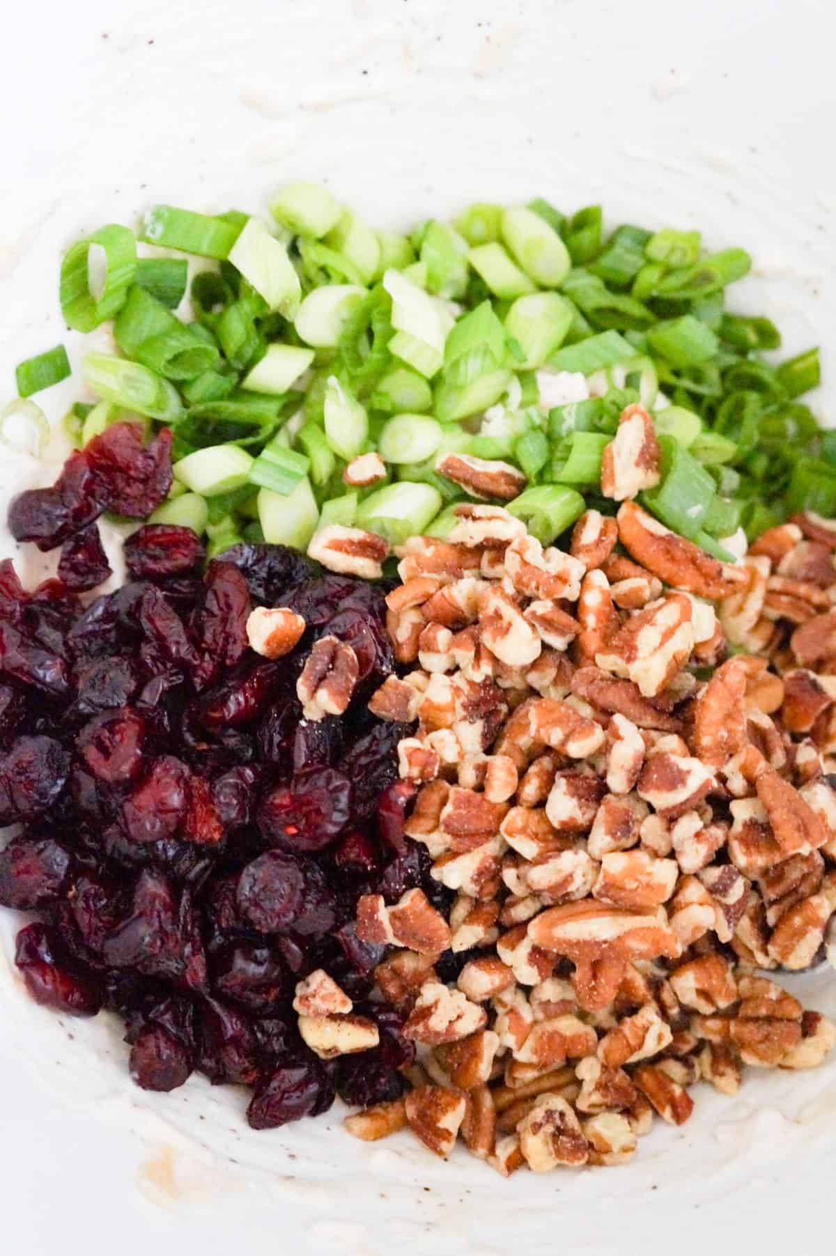 chopped green onions, dried cranberries and pecan pieces on top of chicken salad in a mixing bowl