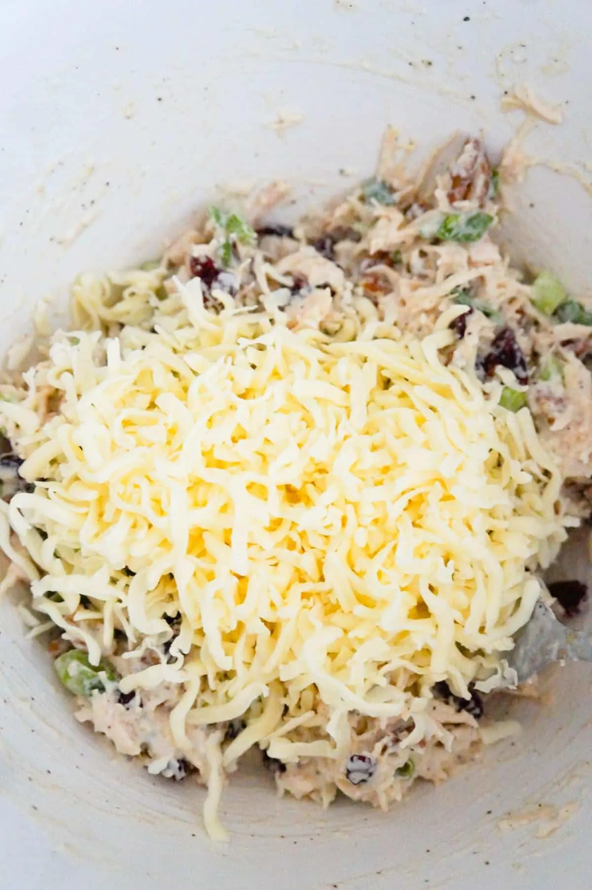 shredded mozzarella cheese on top of chicken salad mixture in a mixing bowl
